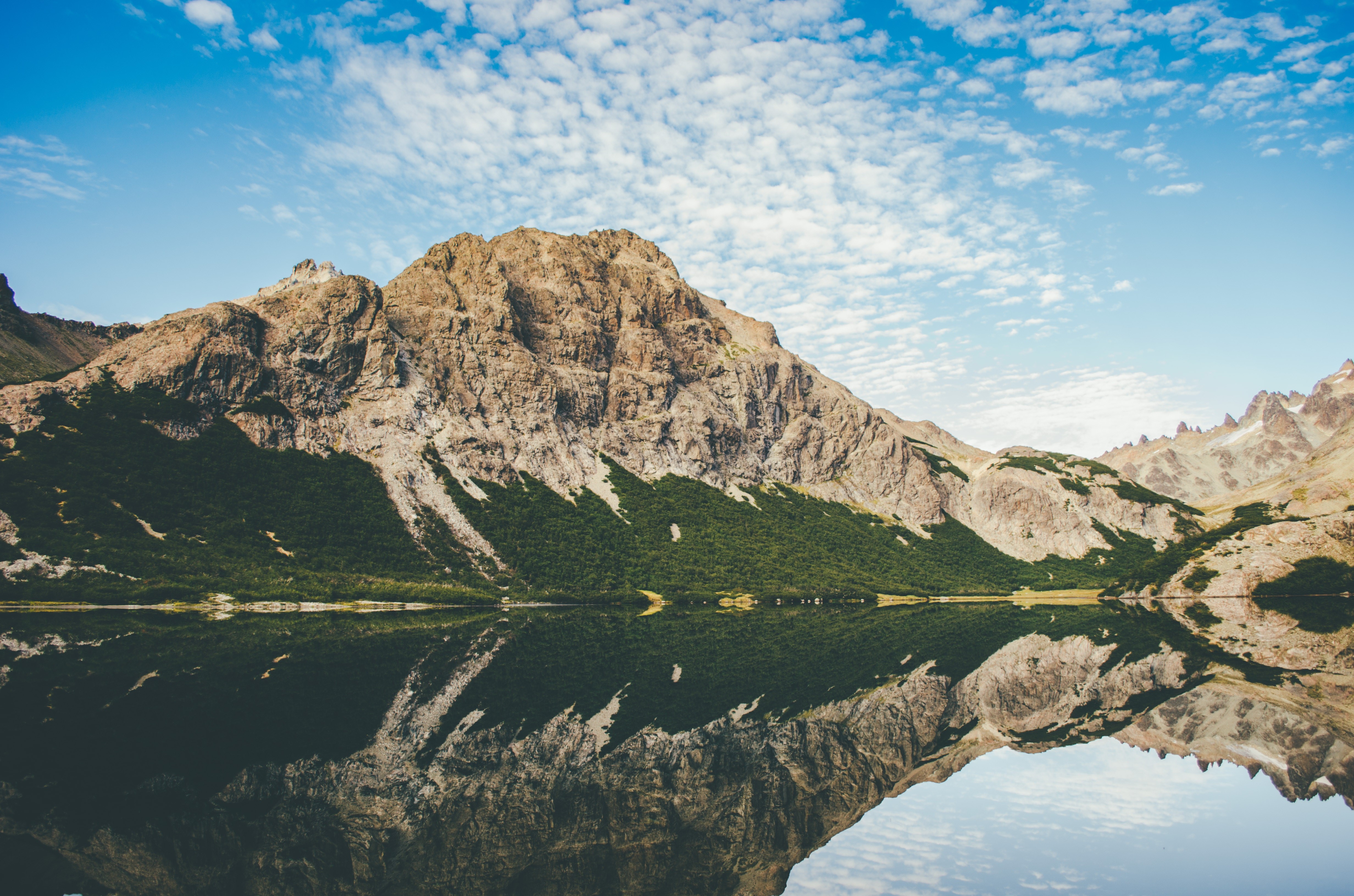 Mountain range reflected in a calm lake under a cloudy sky HD Wallpaper