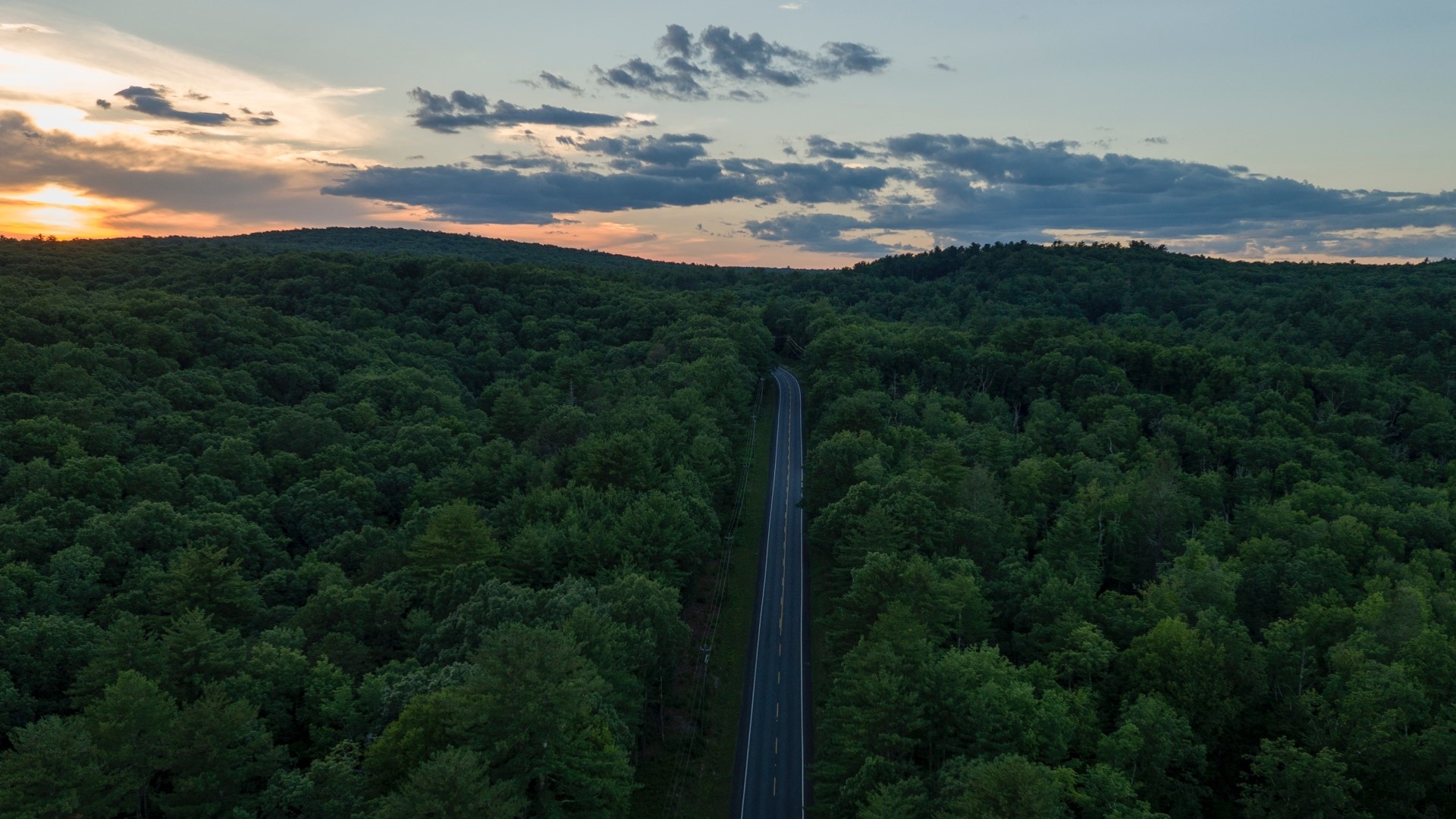 Aerial view of a highway through a forest at sunset HD Wallpaper