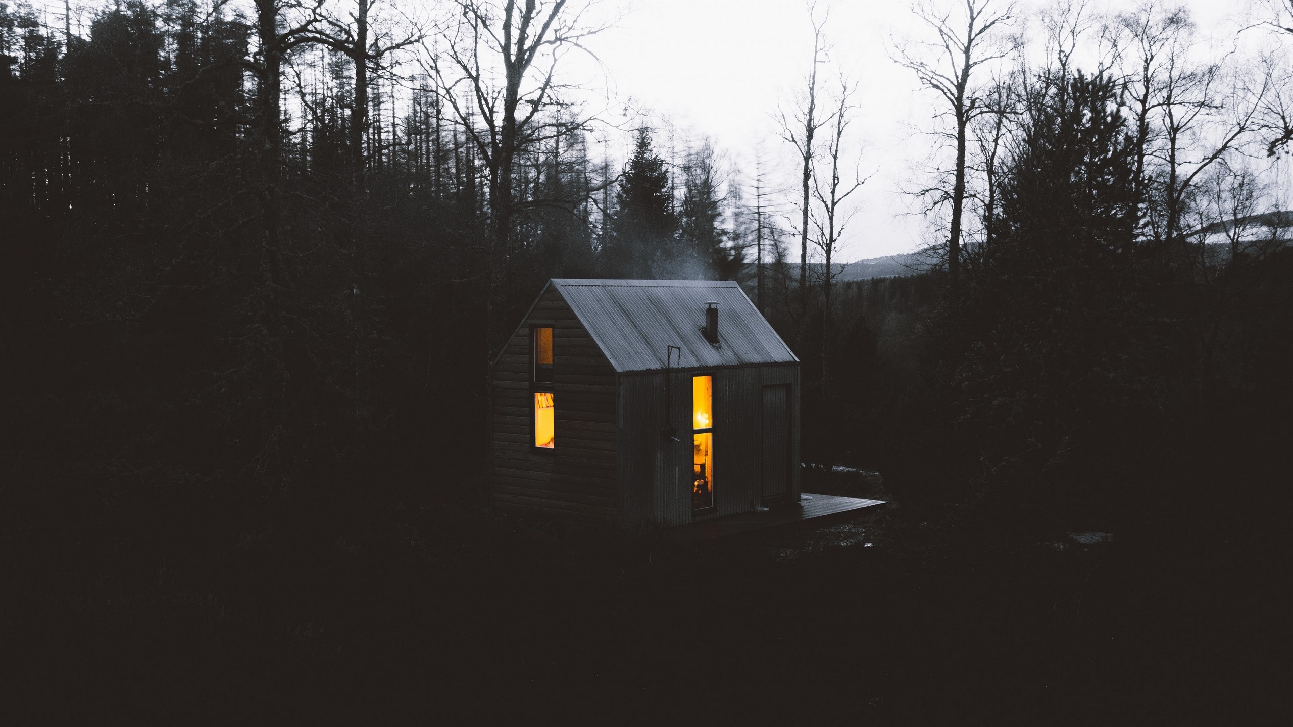Cabin in a dark forest with smoke from chimney HD Wallpaper