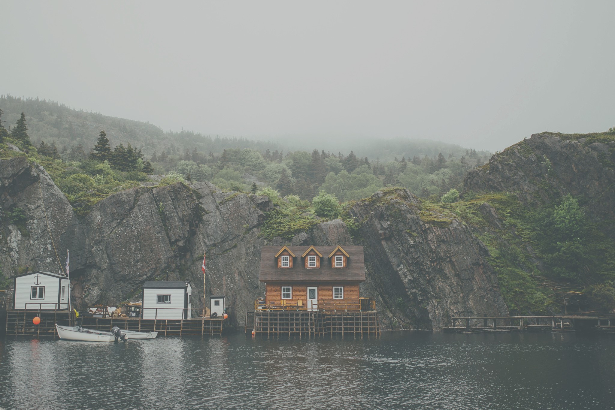 Houses on a pier by rocky cliffs in mist HD Wallpaper