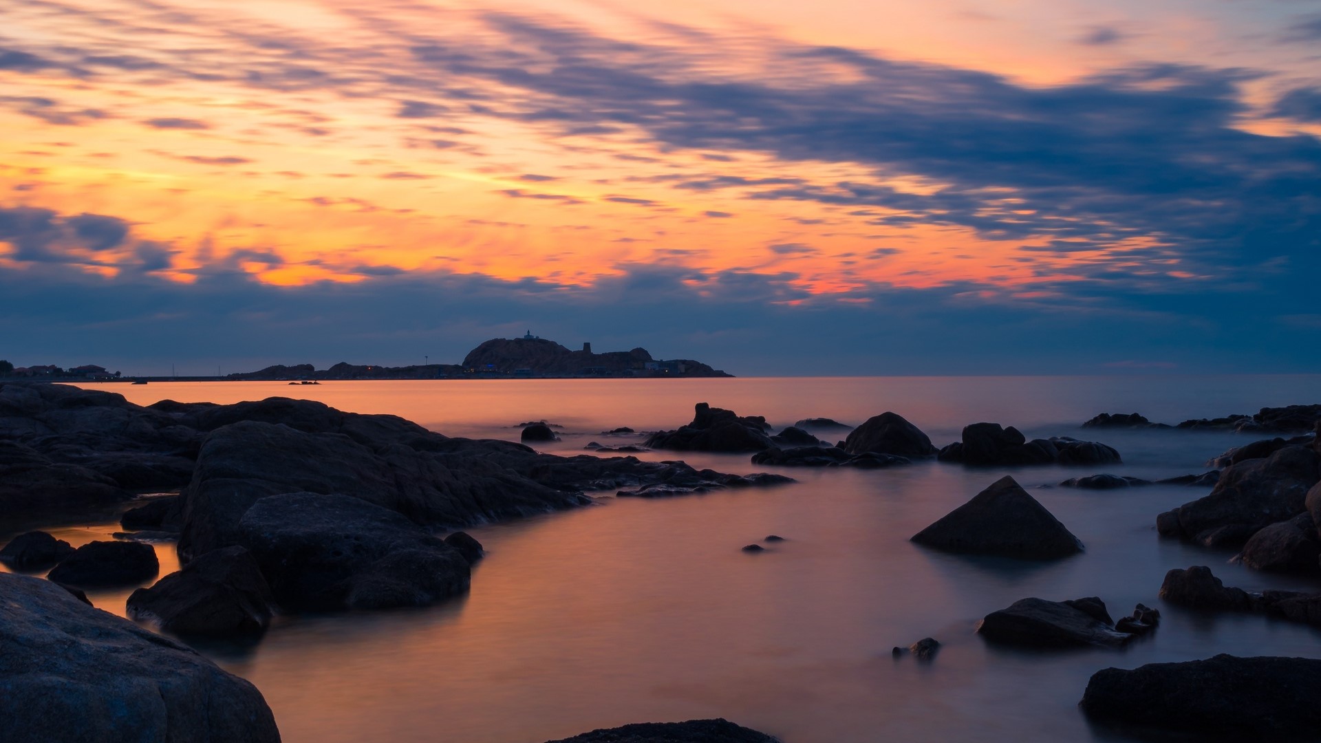 Sunset over the rocky Mediterranean coast with distant island HD Wallpaper