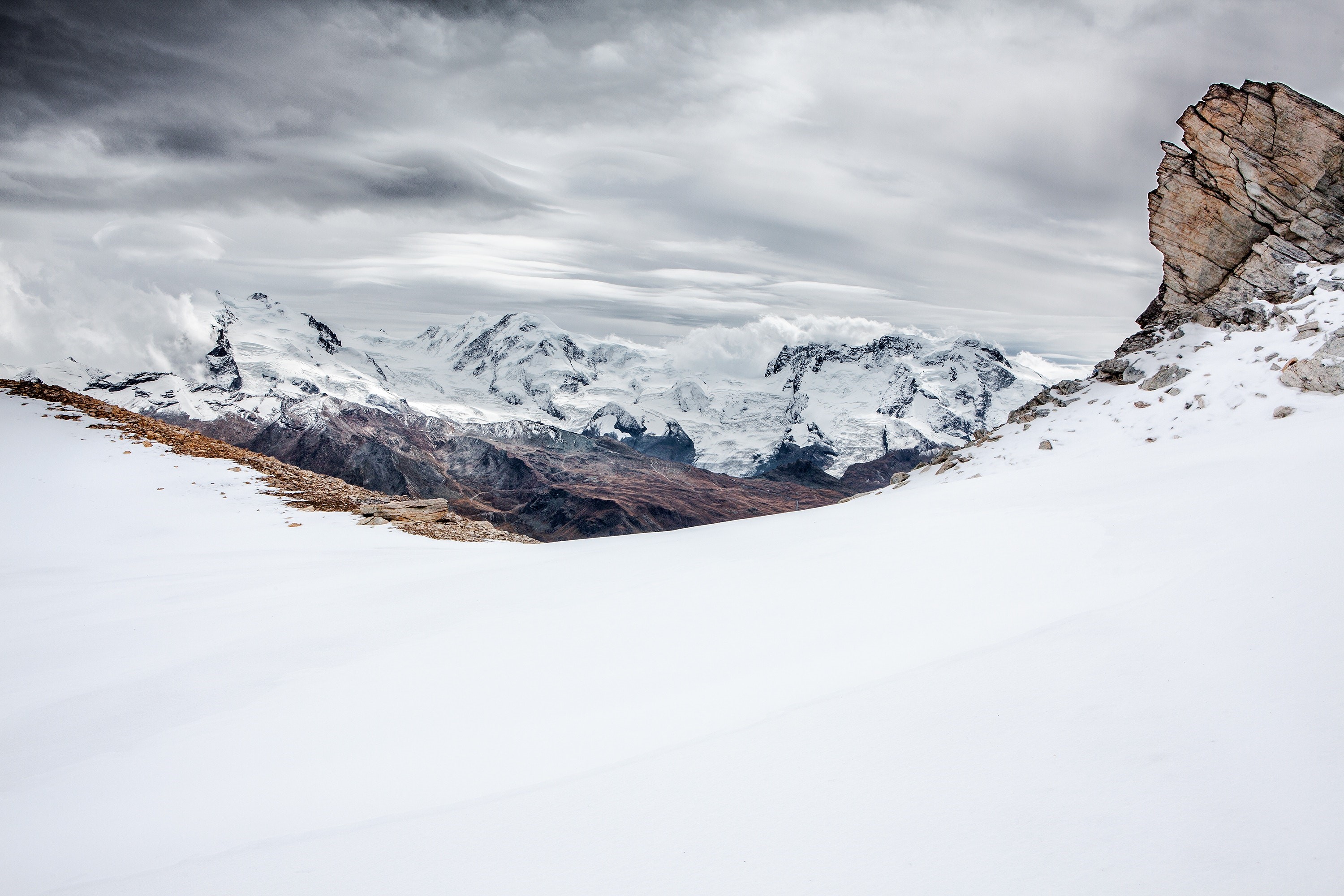 Snow-covered mountains under a cloudy sky HD Wallpaper