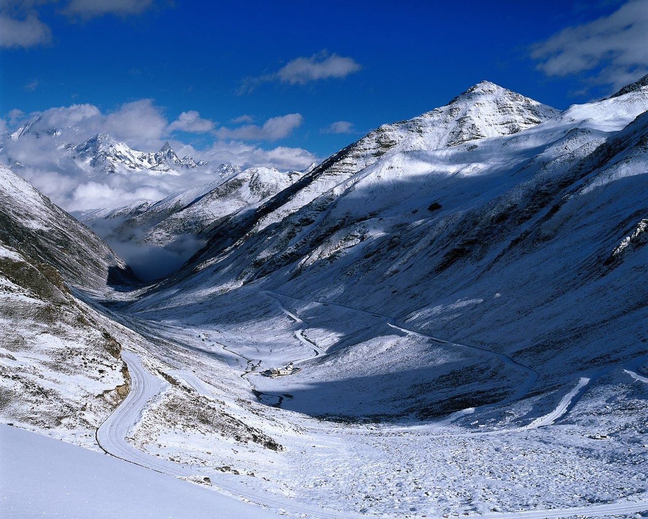 Snowy mountain valley with winding road and clouds HD Wallpaper