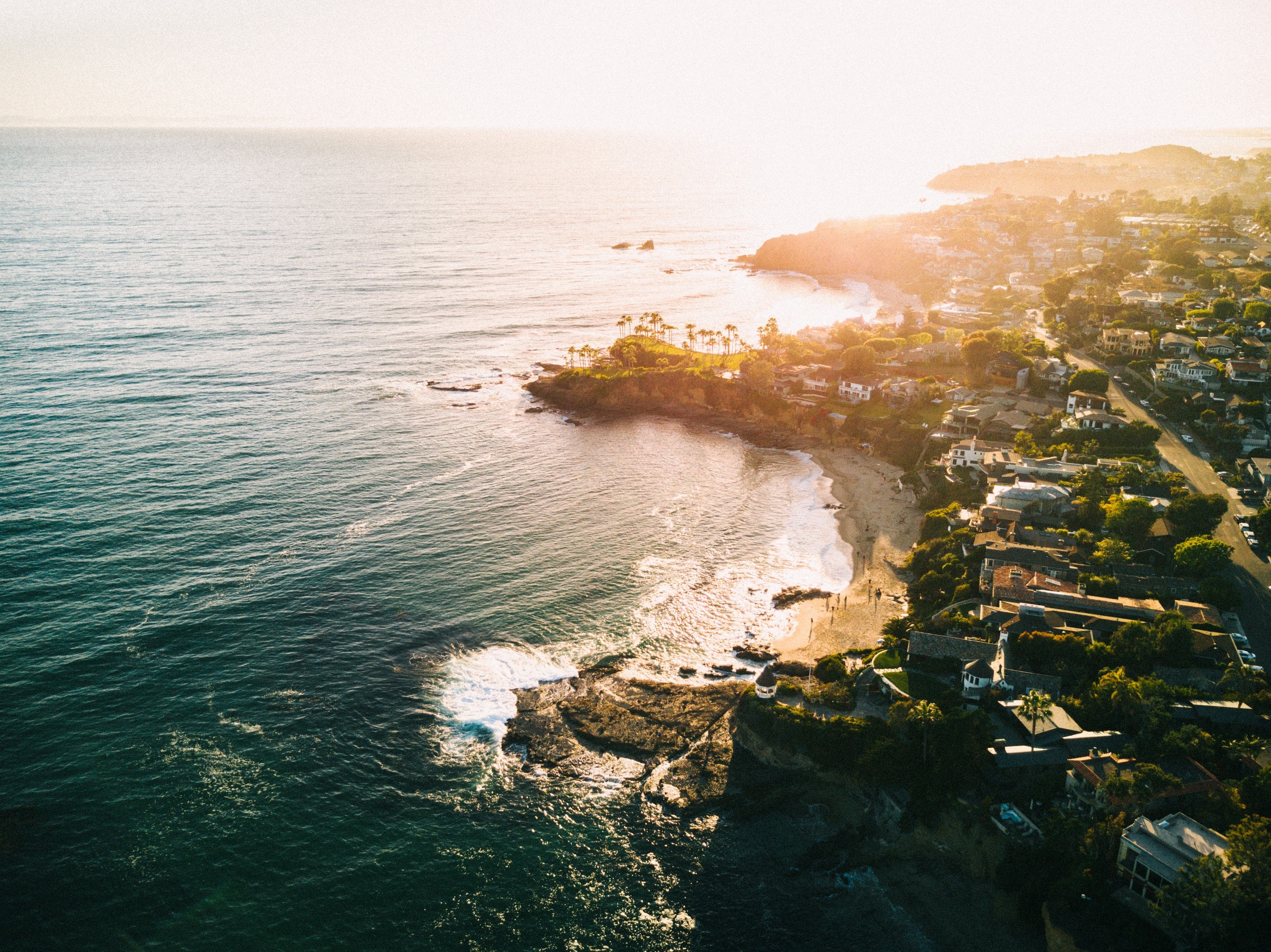 Aerial view of a sunlit coastline with houses and a beach HD Wallpaper