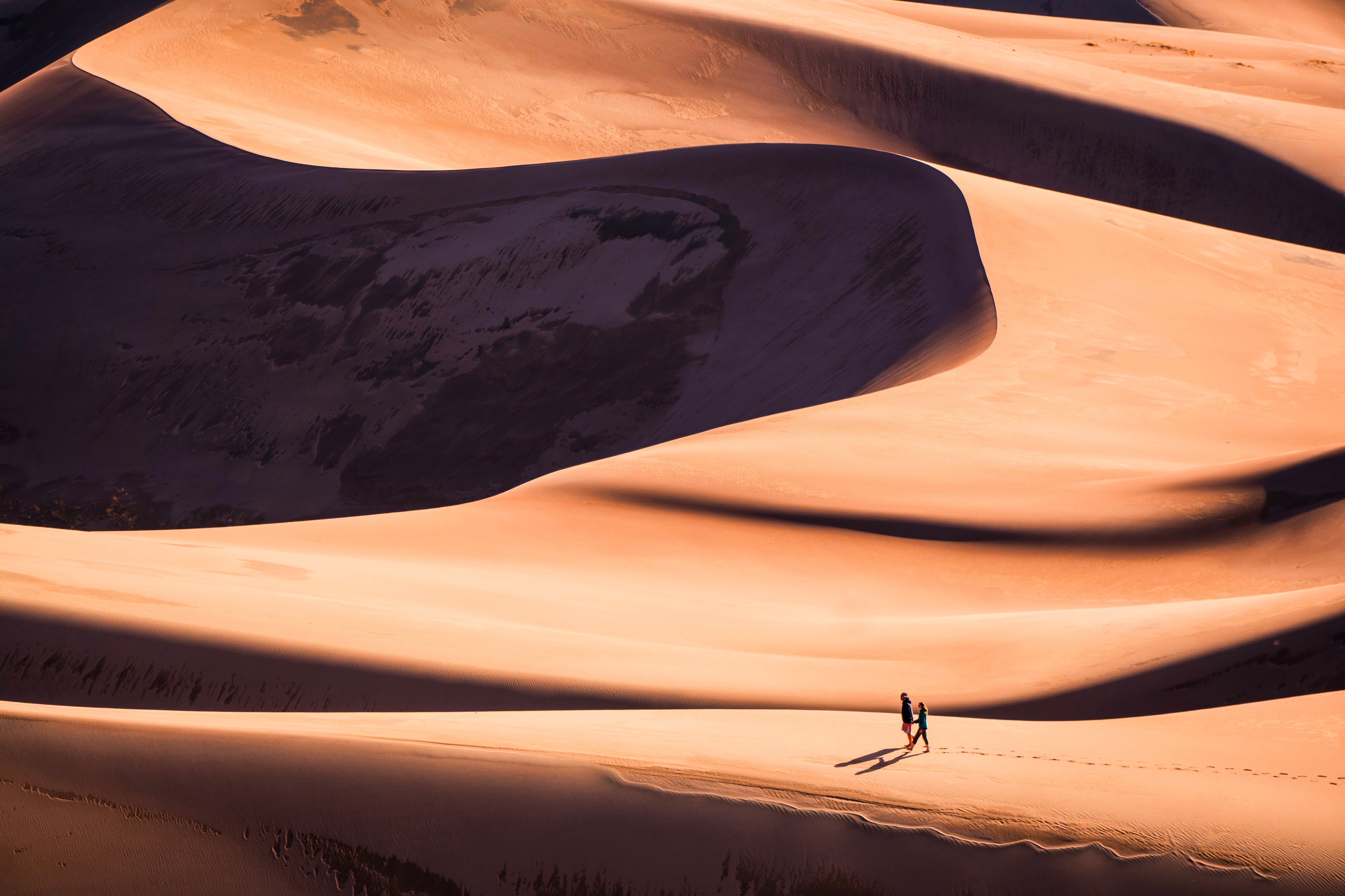 Two people walking on sand dunes HD Wallpaper