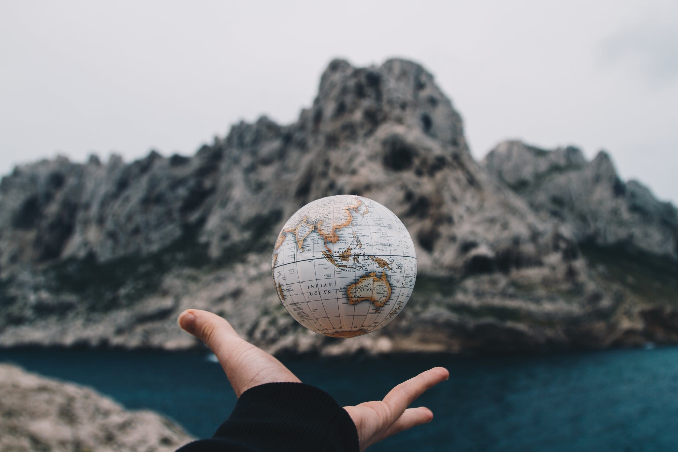 Hand holding a globe with mountains and ocean in background HD Wallpaper
