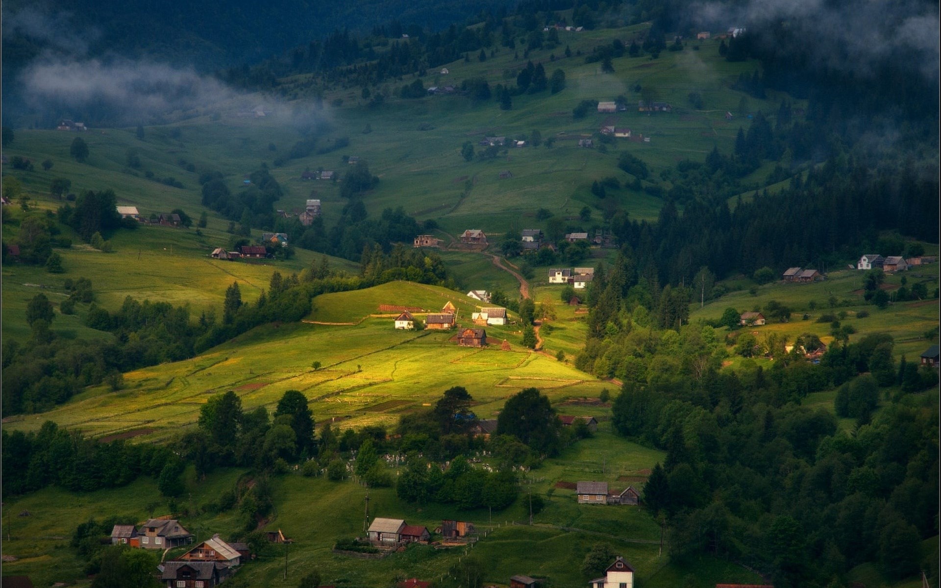 Village nestled in a green mountain valley with mist HD Wallpaper