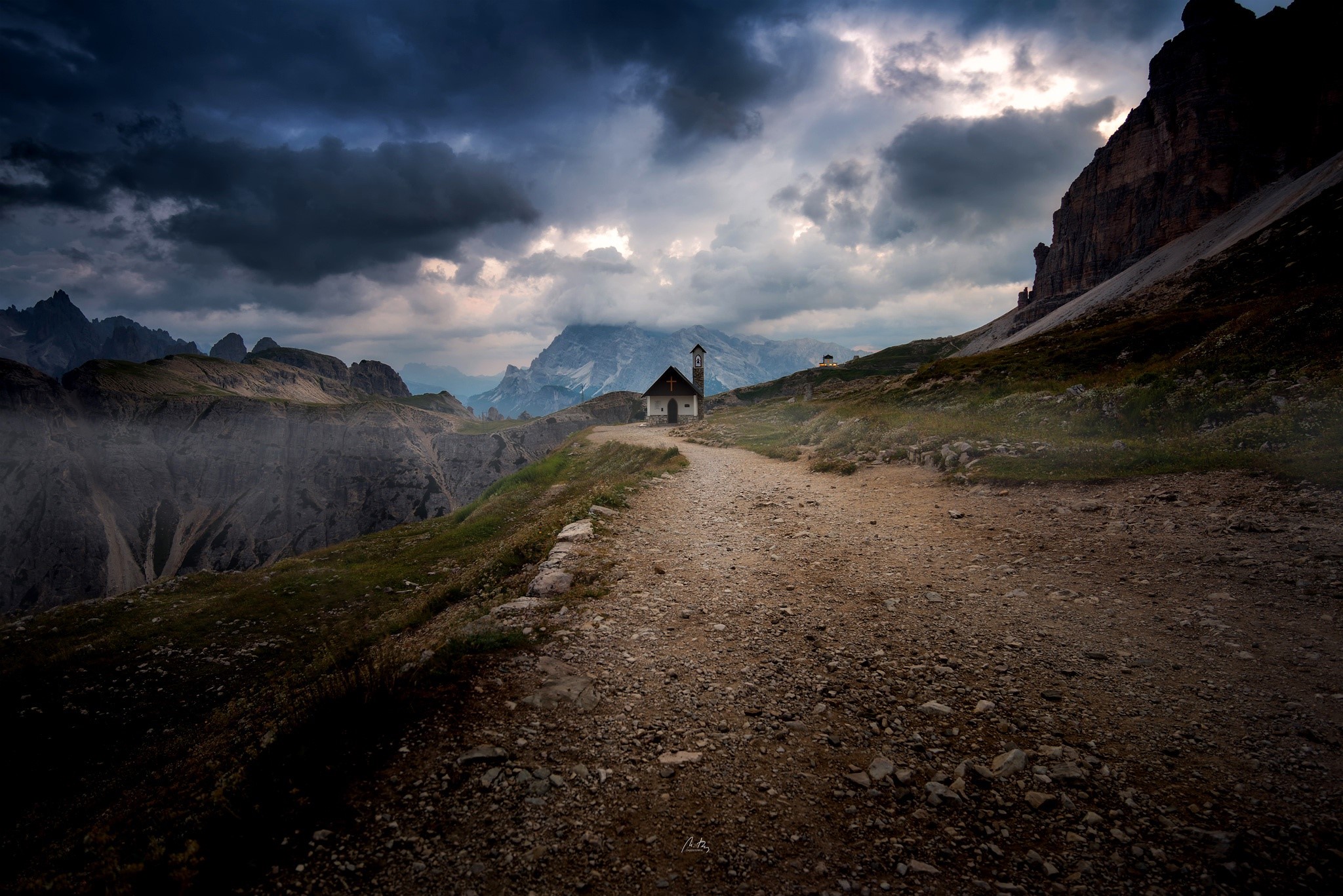 Chapel on a mountain path under dark clouds HD Wallpaper