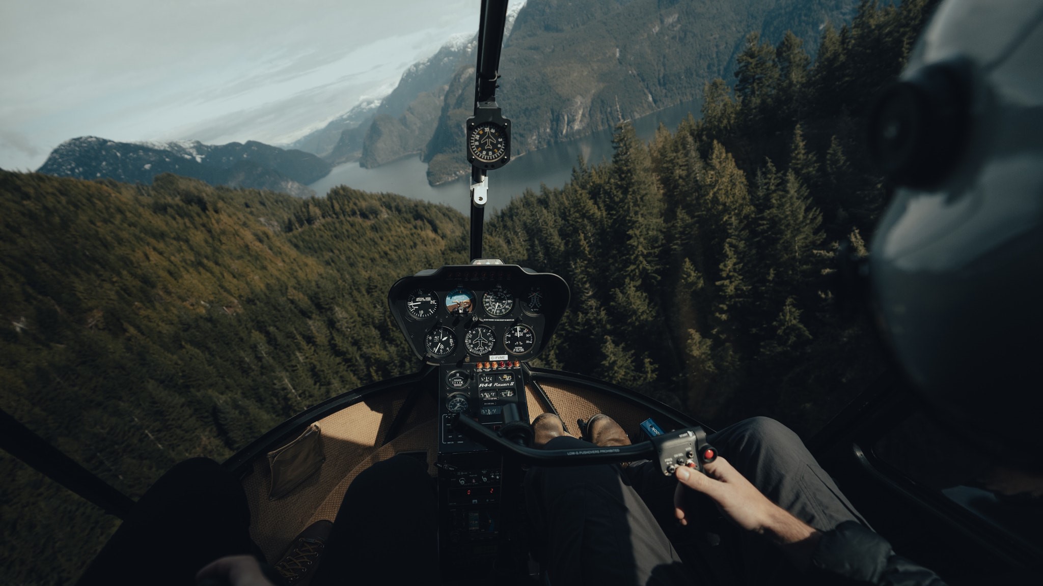 Helicopter cockpit view over forested mountains and water HD Wallpaper