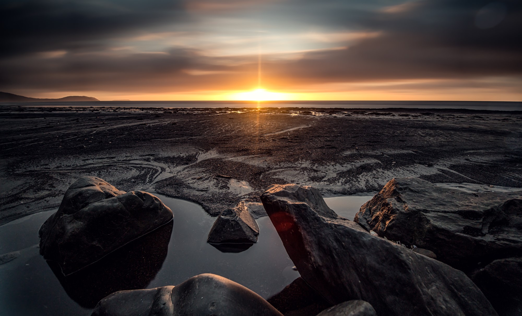Sunset over a rocky beach with calm sea HD Wallpaper
