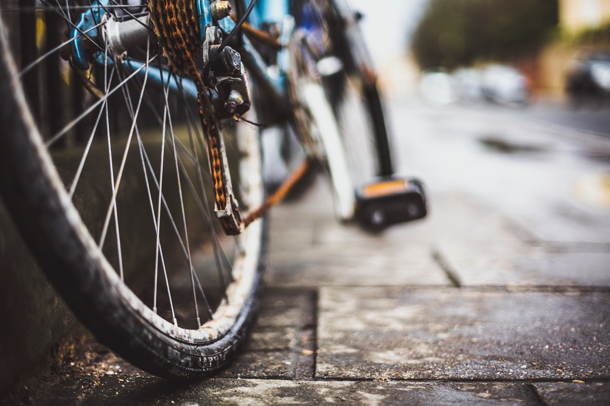 Close-up of a rusty bicycle chain and wheel on a wet pavement HD Wallpaper
