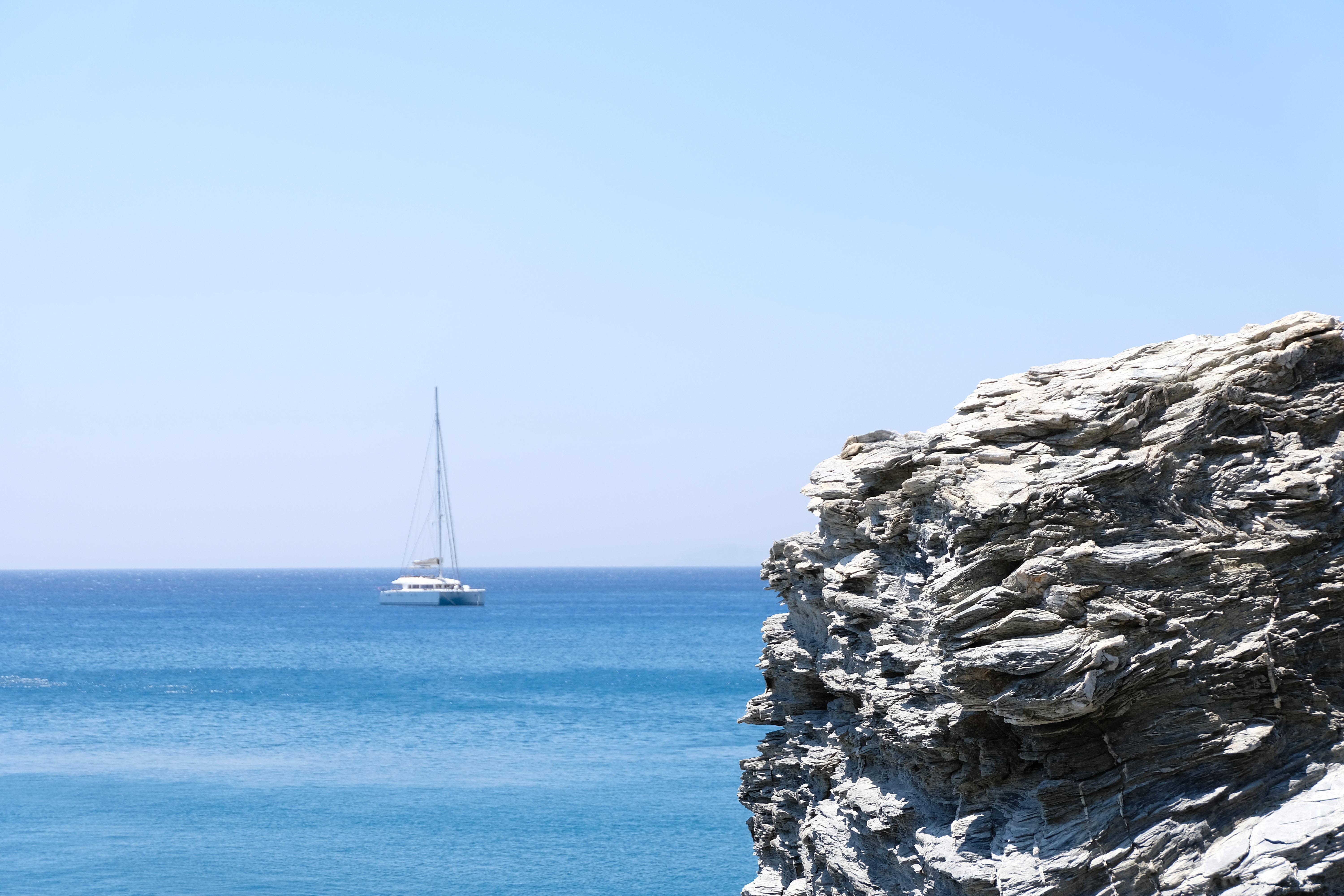 Catamaran sailing in the blue sea near a rocky shore HD Wallpaper