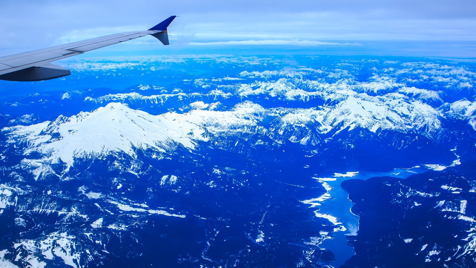 Airplane wing over snowy mountains and lake HD Wallpaper