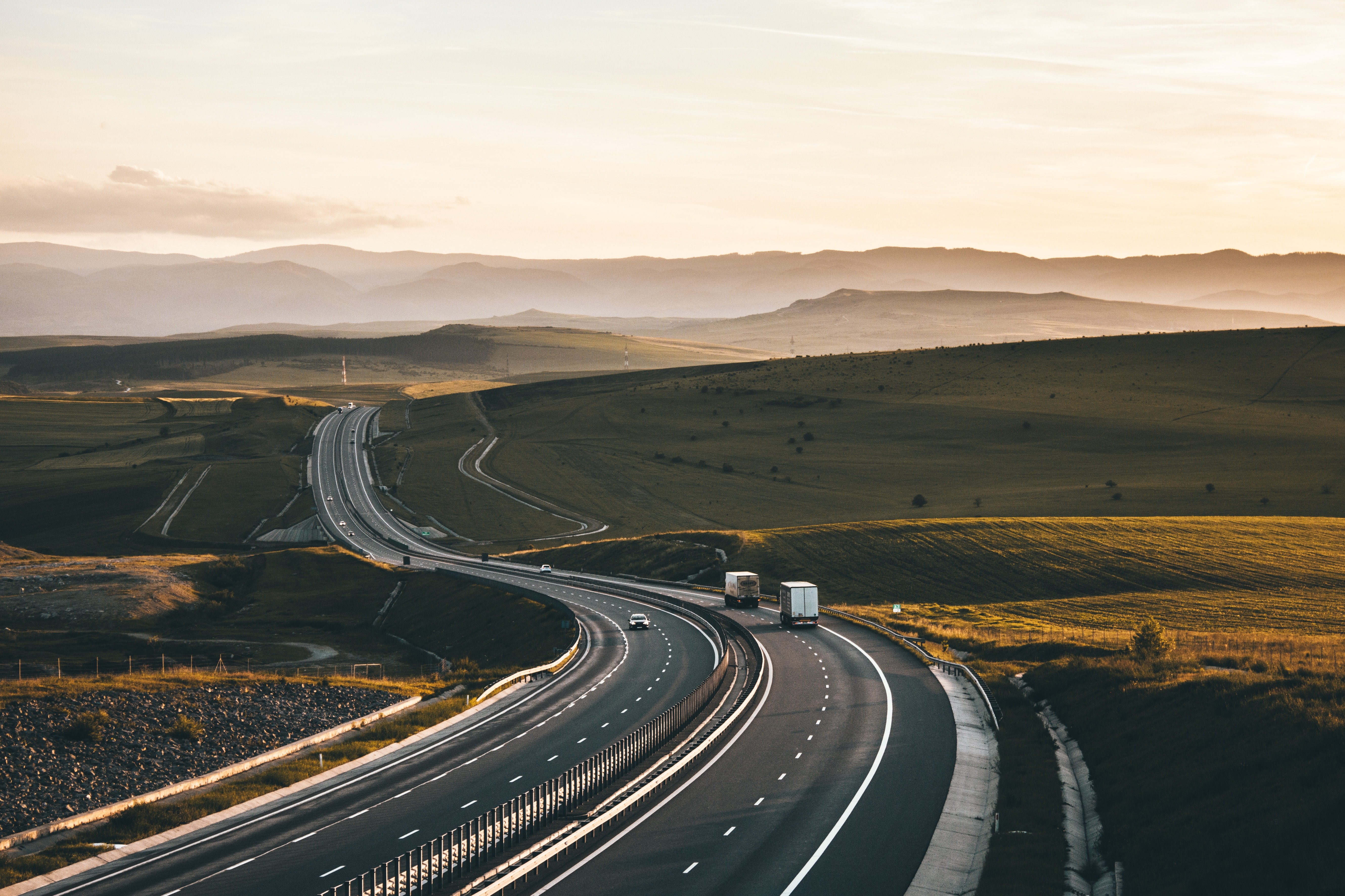 Highway landscape with trucks and hills at sunset HD Wallpaper