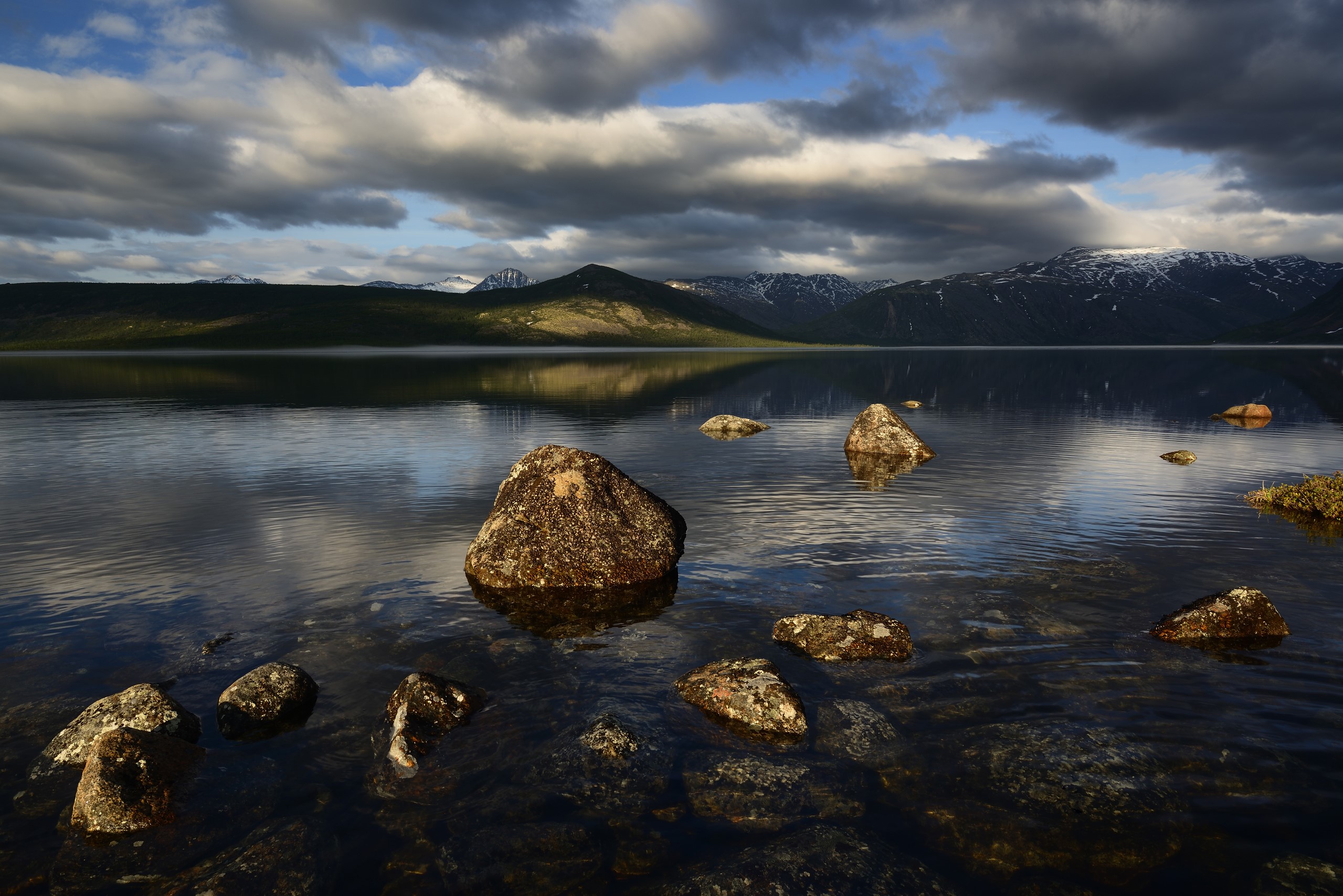 Lake with rocks and mountains under cloudy sky HD Wallpaper