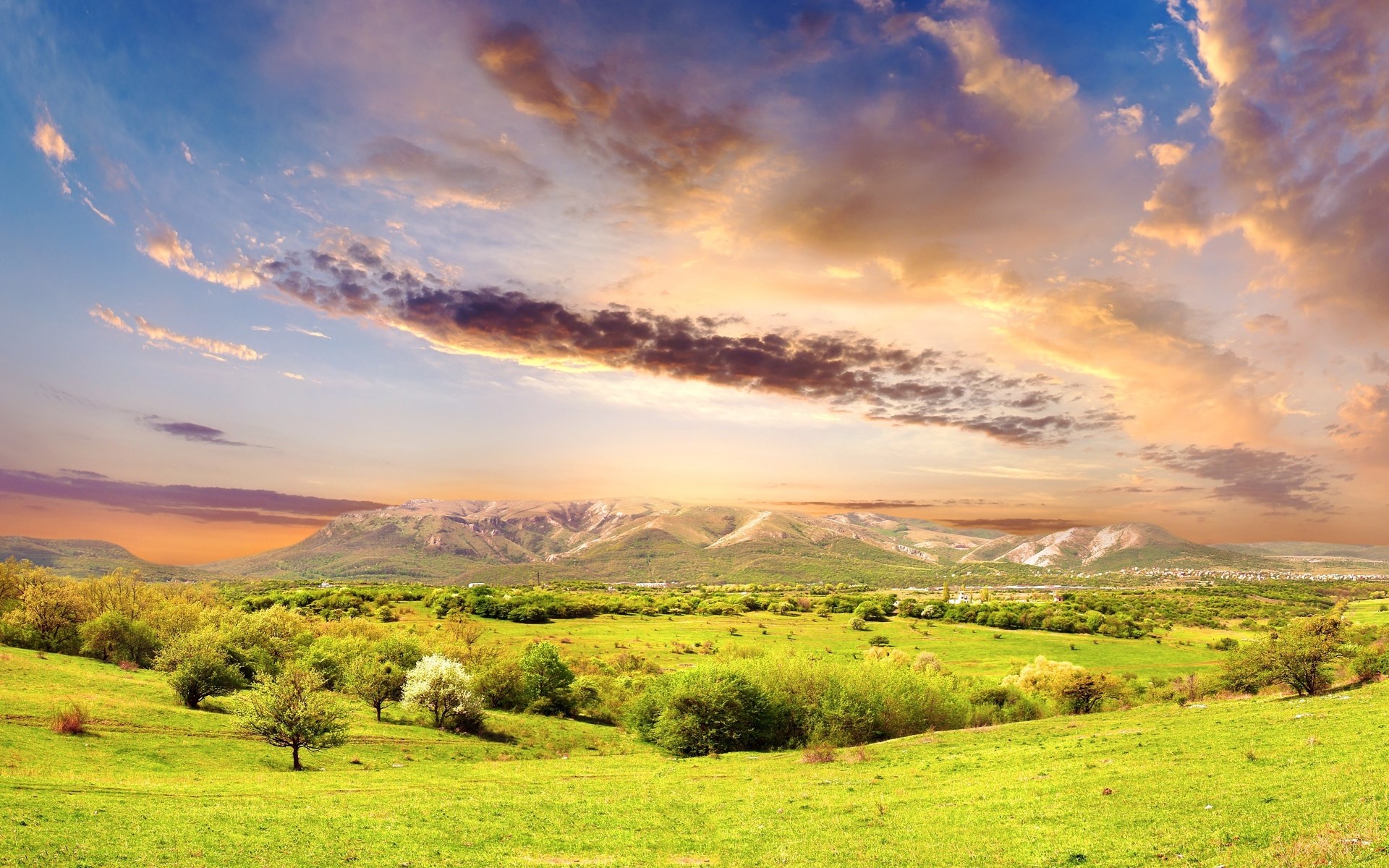 Green rolling hills and mountains under a dramatic sky HD Wallpaper