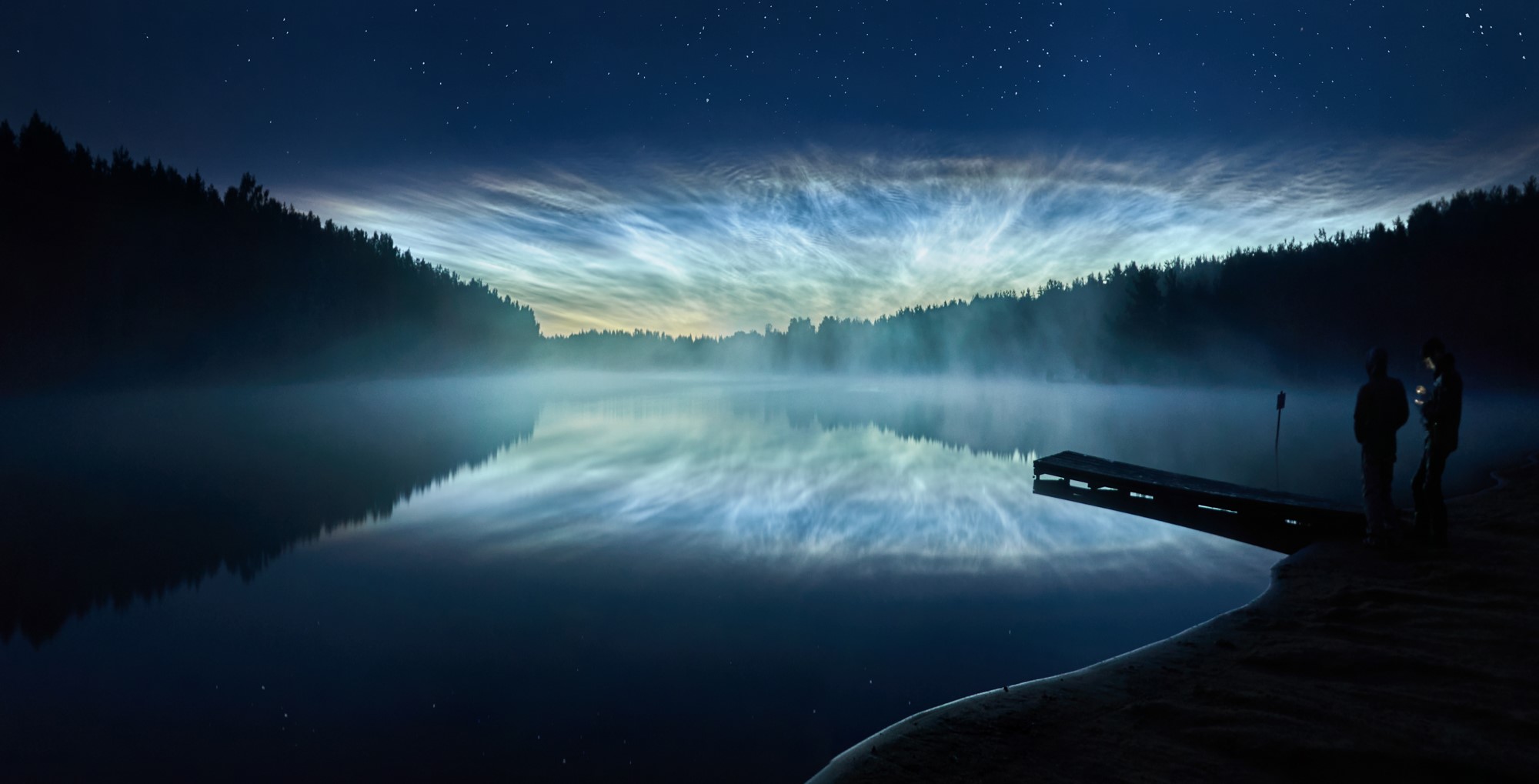 Noctilucent clouds over a lake at night with people on a pier HD Wallpaper