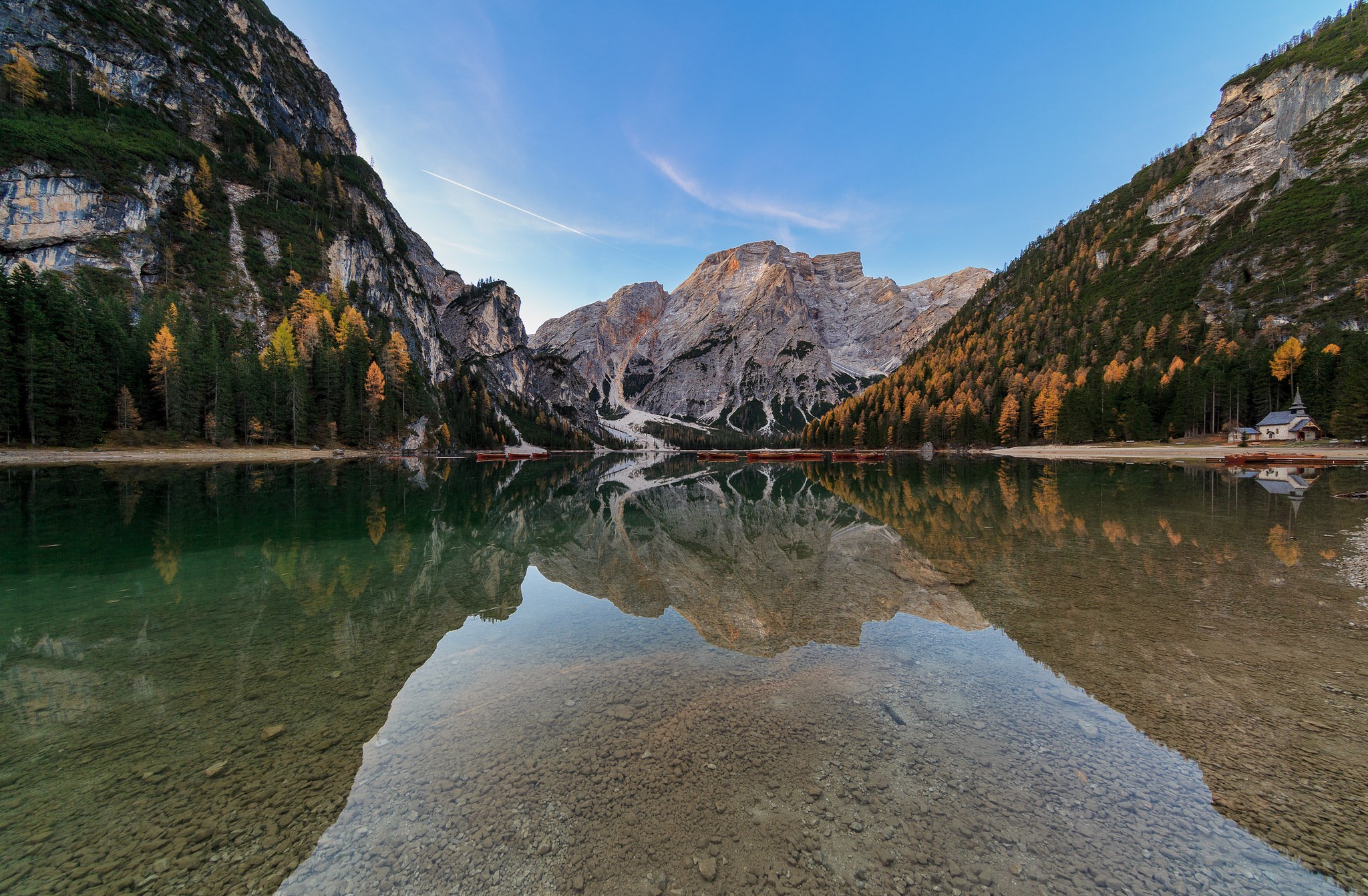 Mountains reflecting in a calm lake with trees and a small building HD Wallpaper