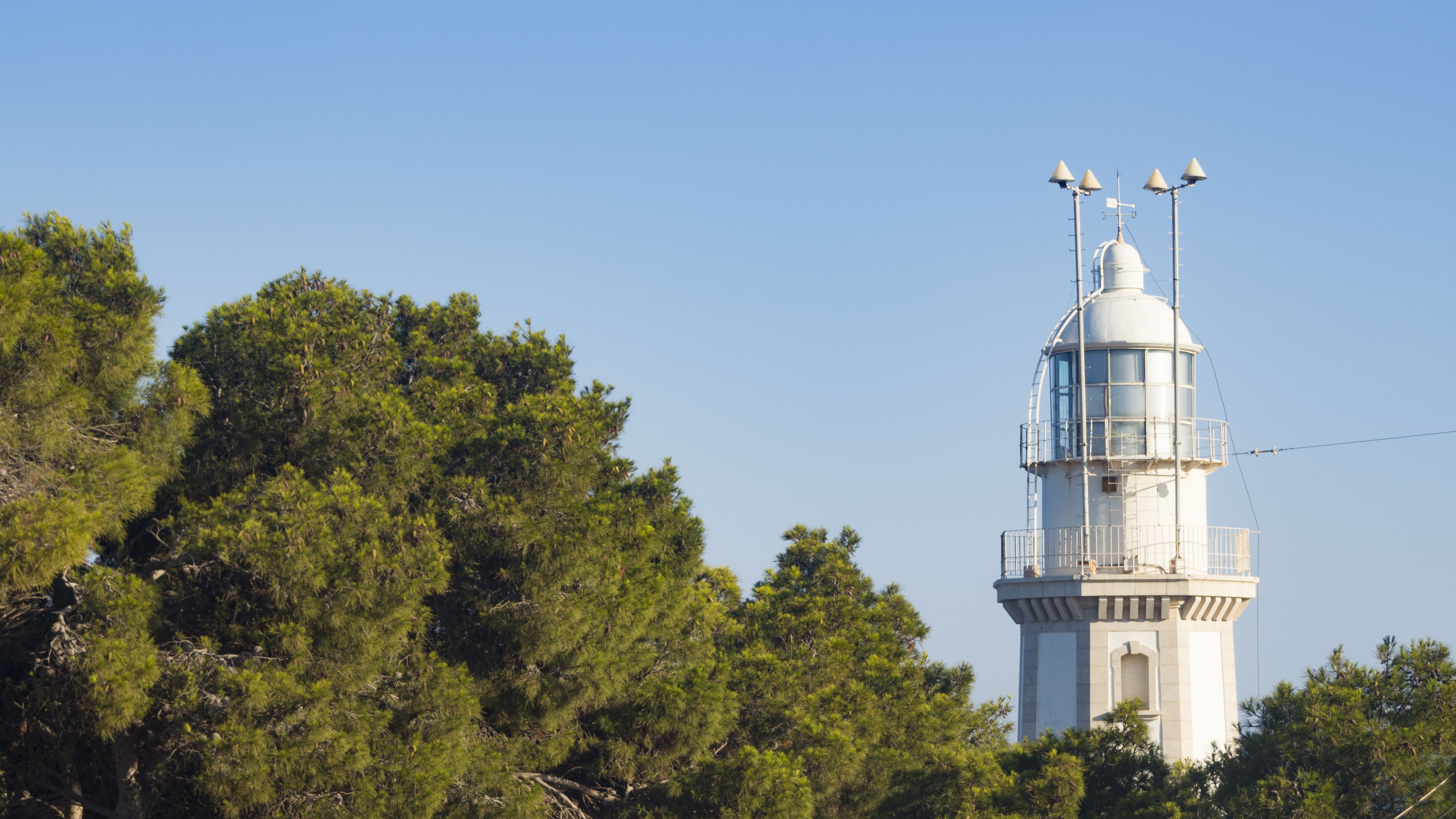 White lighthouse surrounded by green trees under a clear blue sky HD Wallpaper