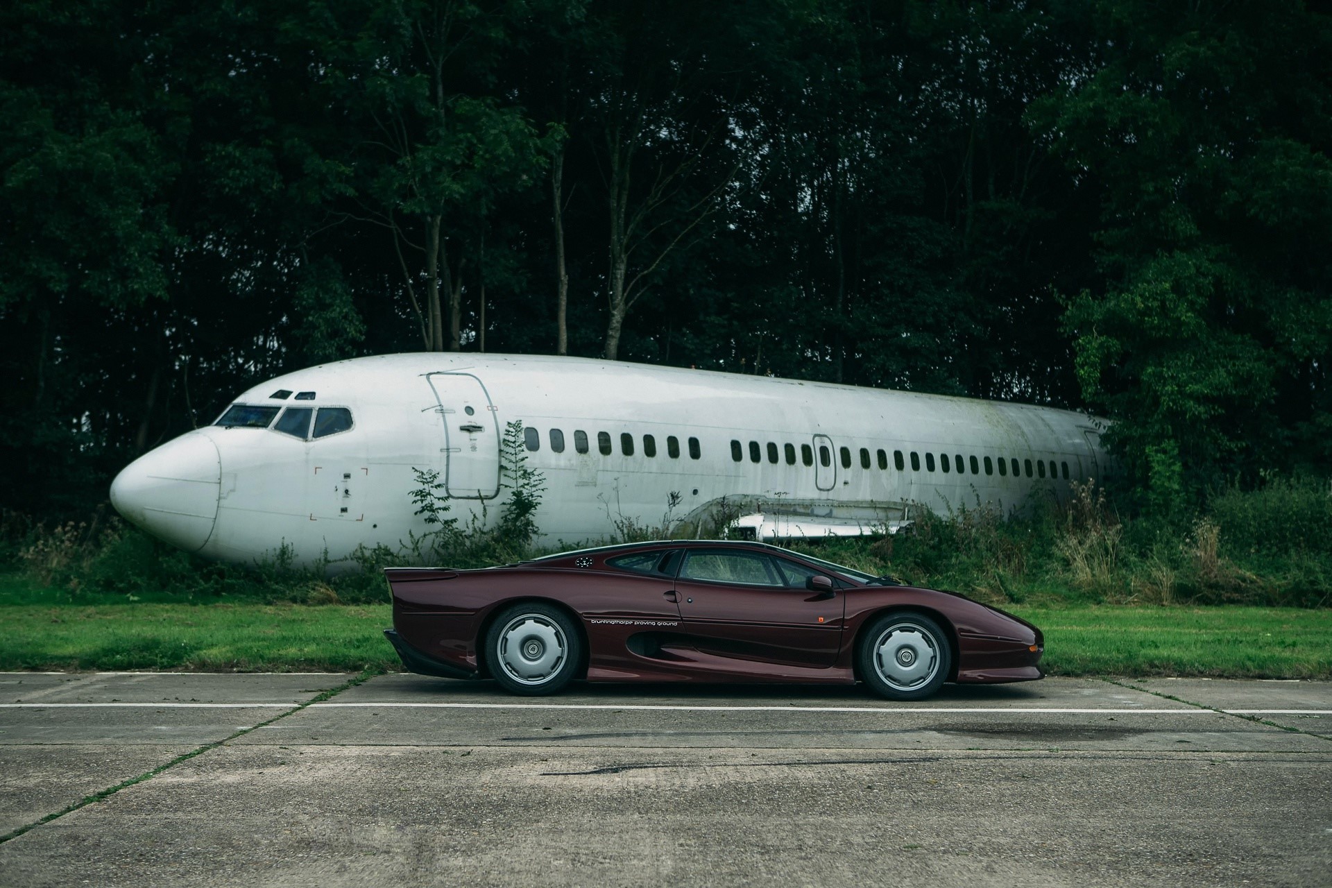 Jaguar XJ220S and abandoned Boeing 737 in forest HD Wallpaper