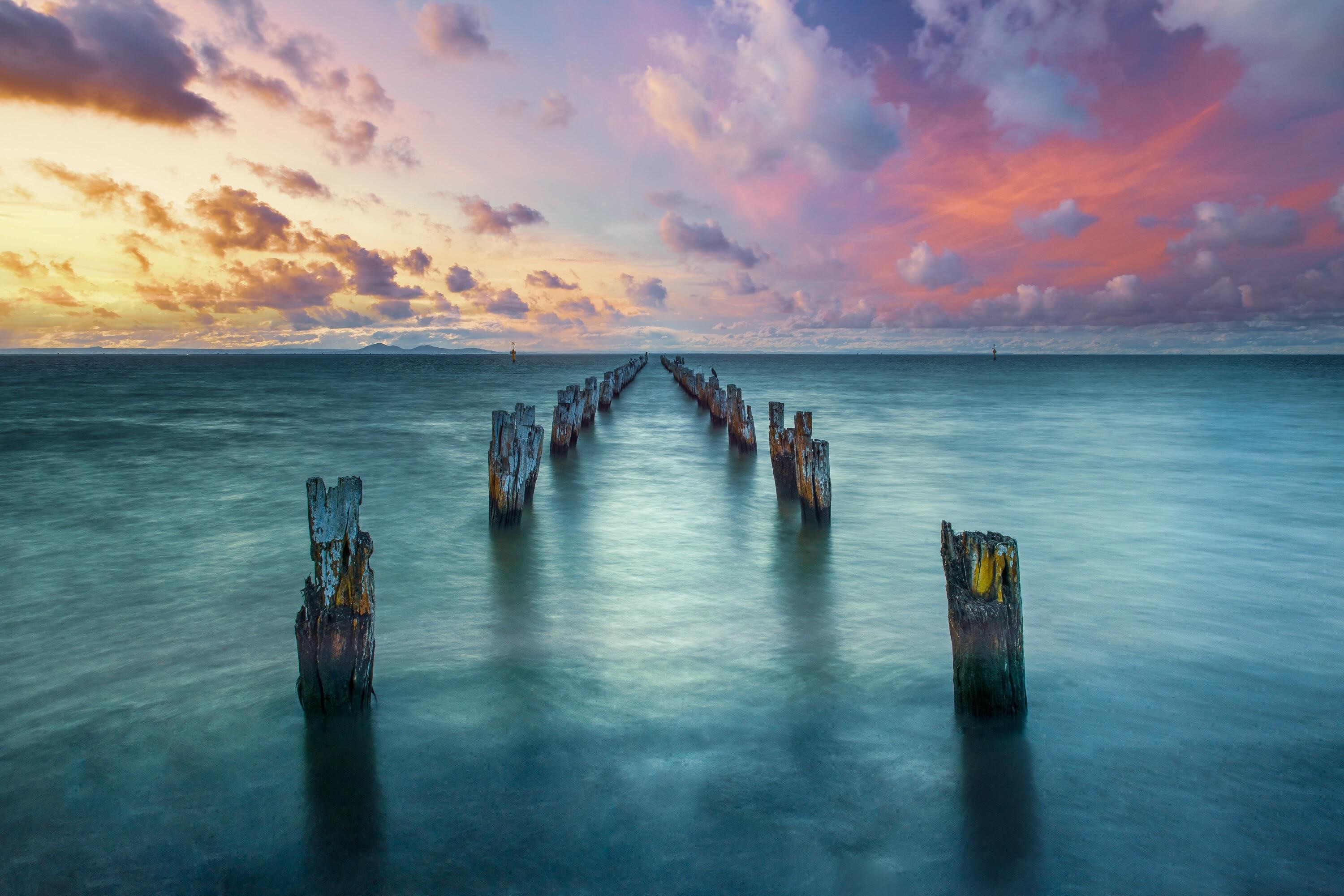 Old wooden jetty posts in the sea at sunset HD Wallpaper