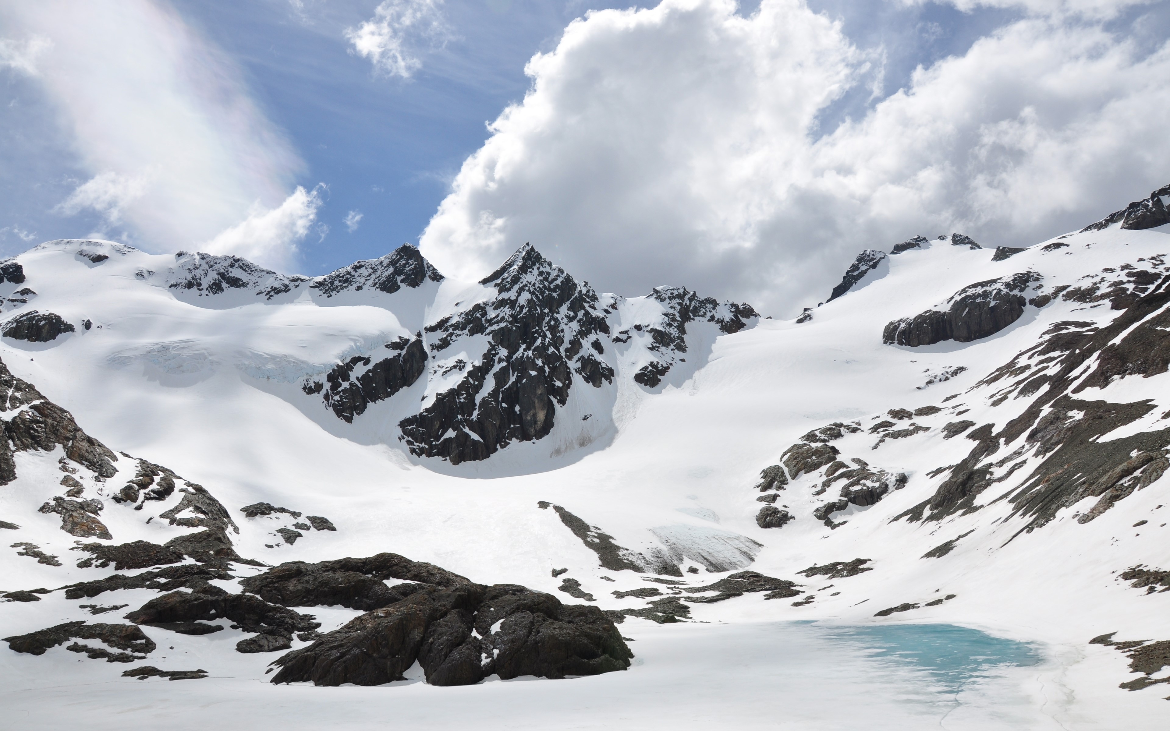 Snowy mountains with clouds and a small lake HD Wallpaper