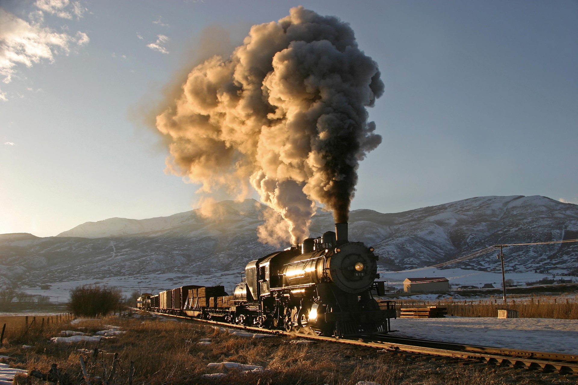 Steam locomotive pulling cargo train through snowy mountains HD Wallpaper