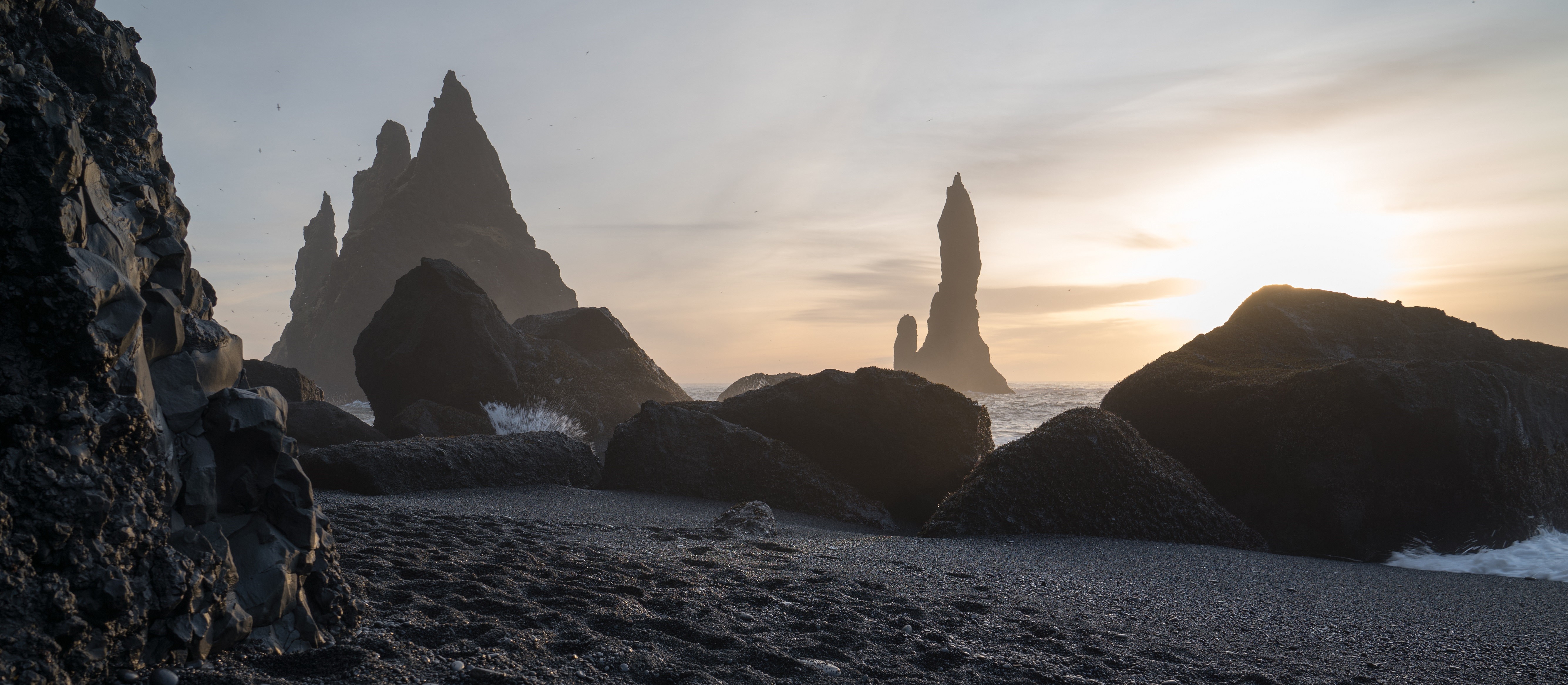 Black sand beach with rock formations at sunset HD Wallpaper