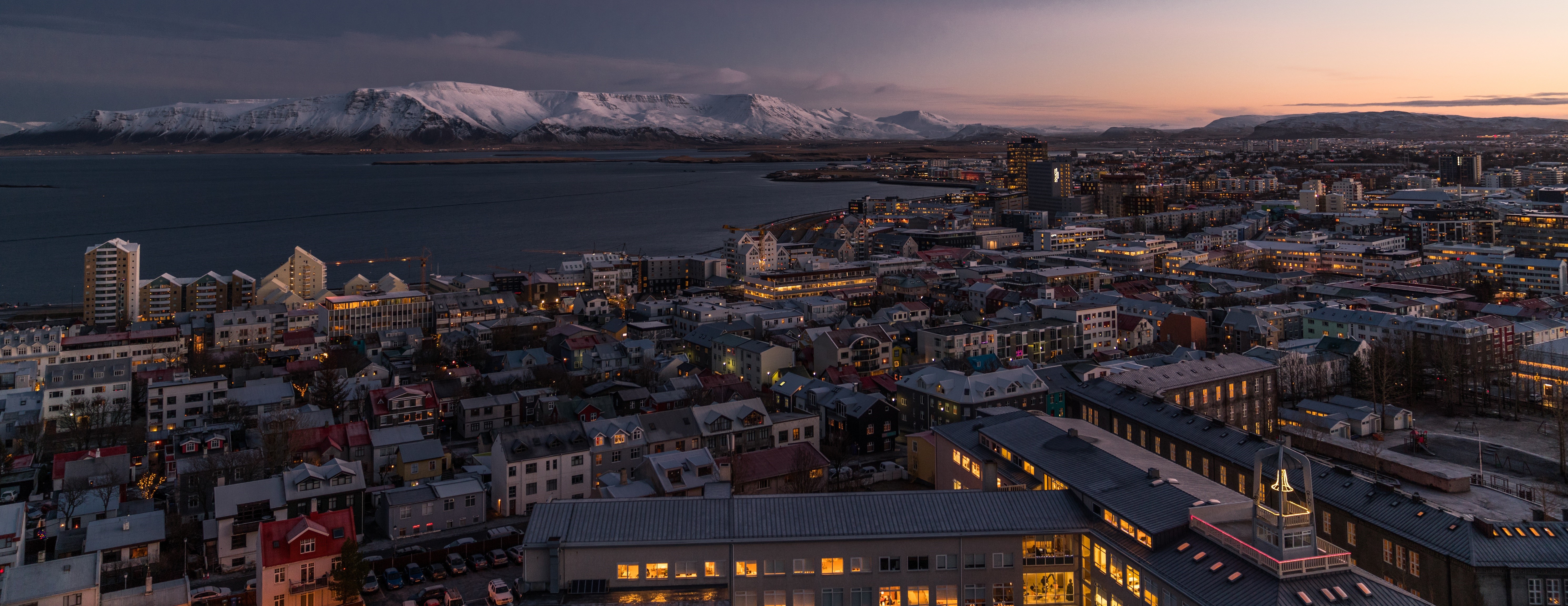 Reykjavik cityscape at sunset with snow-capped mountains HD Wallpaper