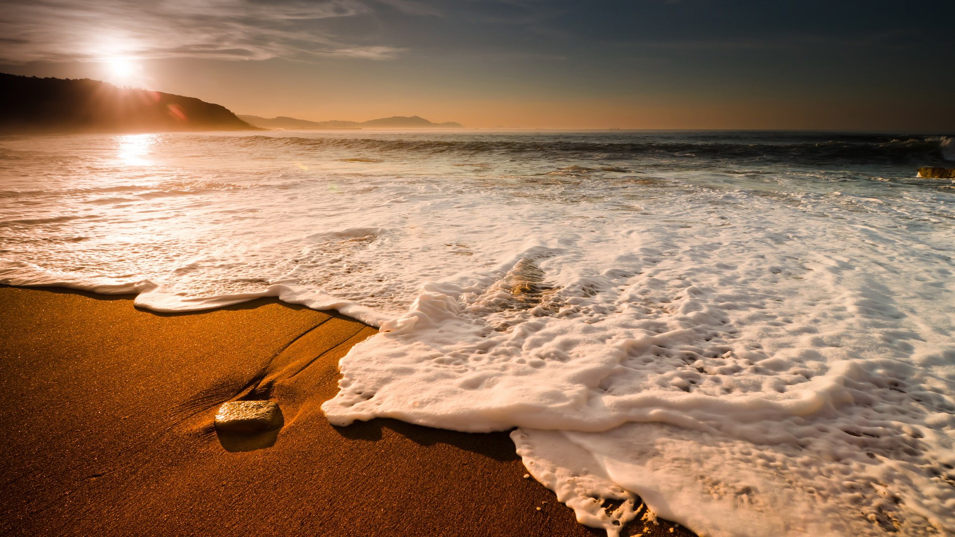 Sunset over a beach with waves crashing on the shore HD Wallpaper