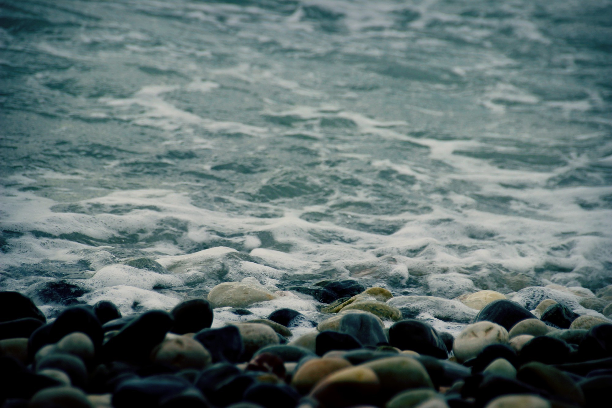 Ocean waves washing over stones on a beach HD Wallpaper