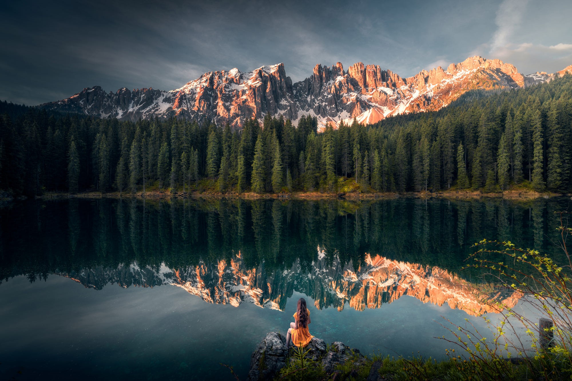 Woman sitting by a lake with mountains and forest reflection HD Wallpaper