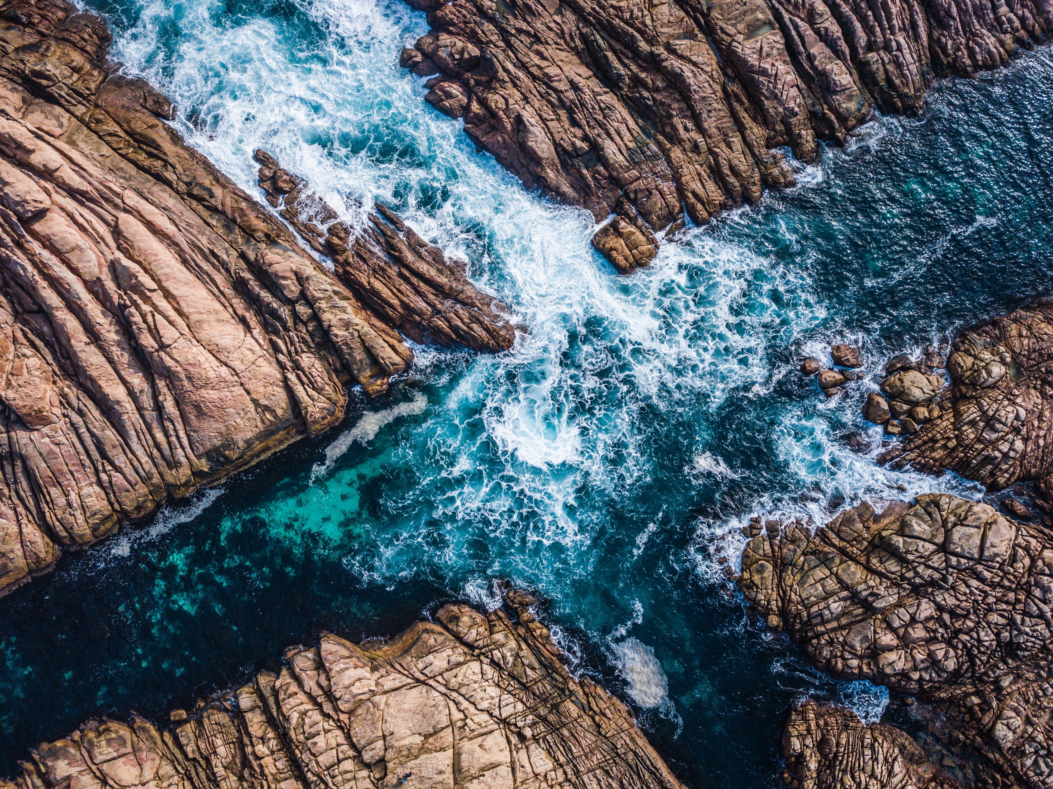 Aerial view of ocean waves crashing on rocky coastline HD Wallpaper