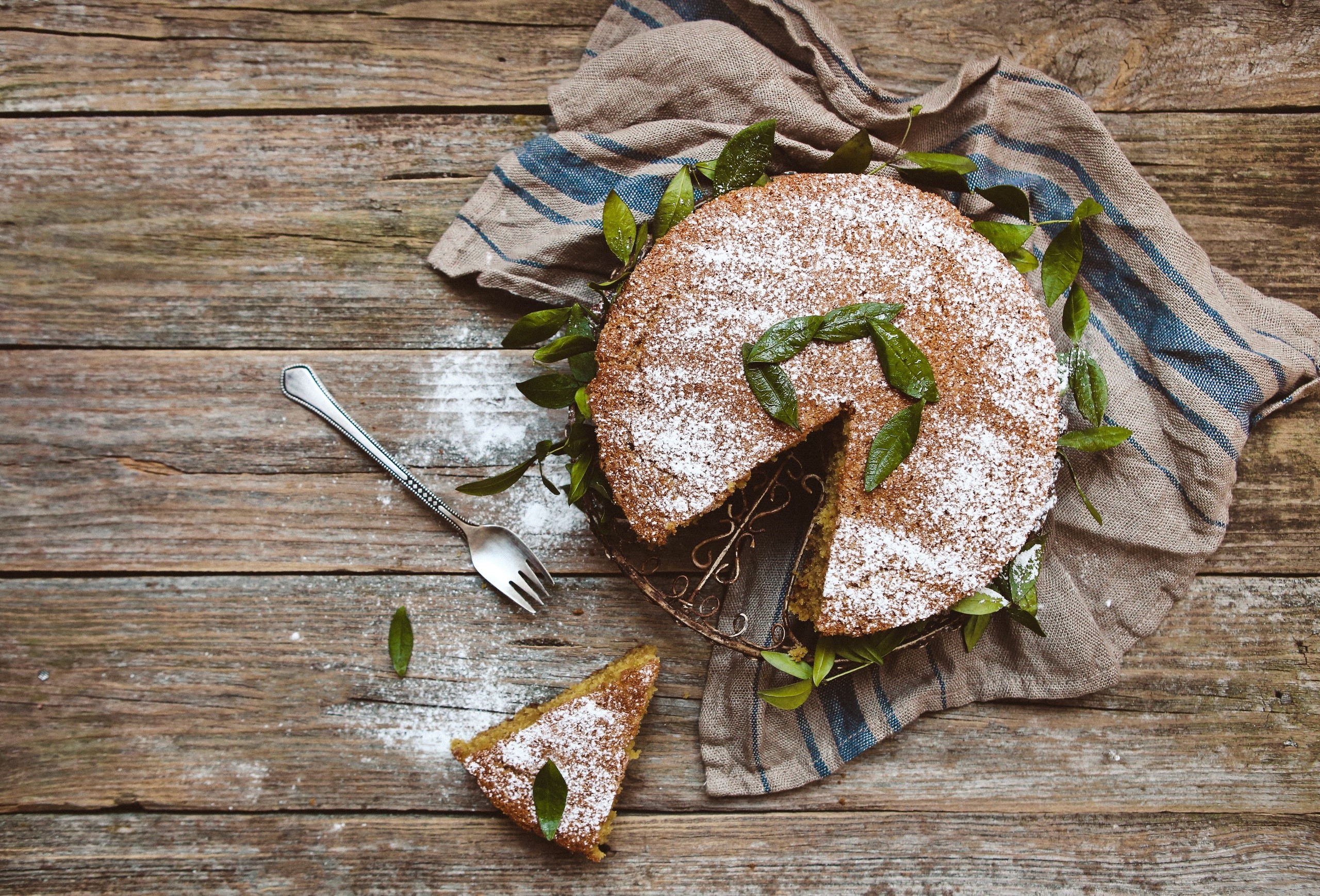 Cake with powdered sugar and leaves on a wooden table HD Wallpaper