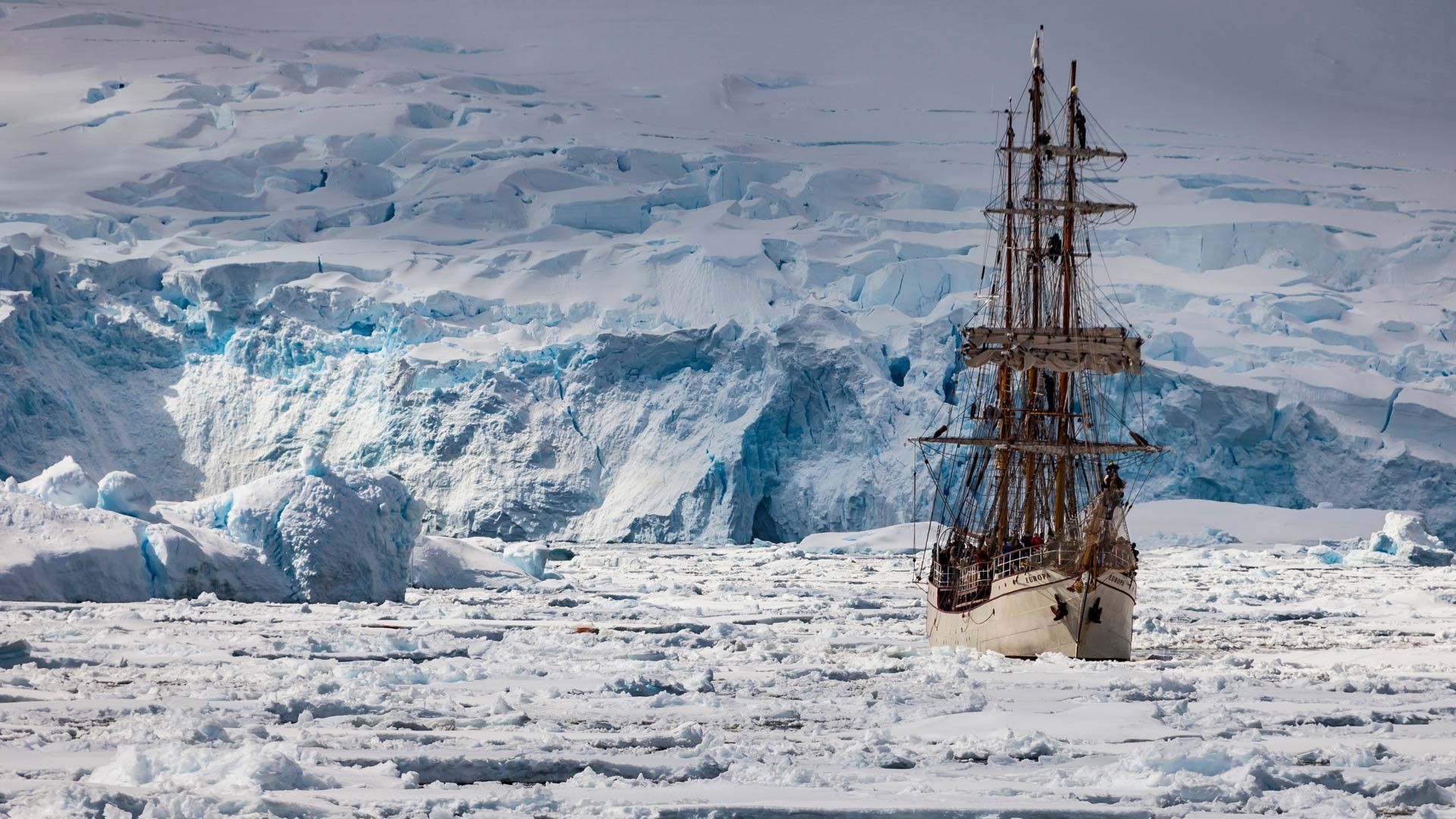 Tall ship sailing through icy waters near a glacier HD Wallpaper