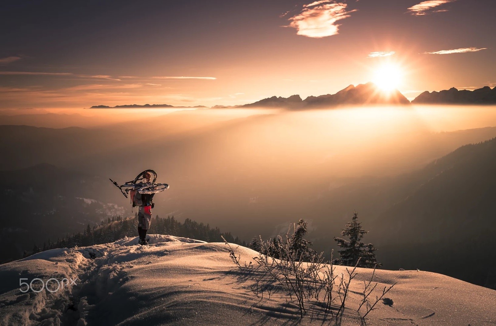 Man carrying bicycle on snowy mountain at sunset HD Wallpaper
