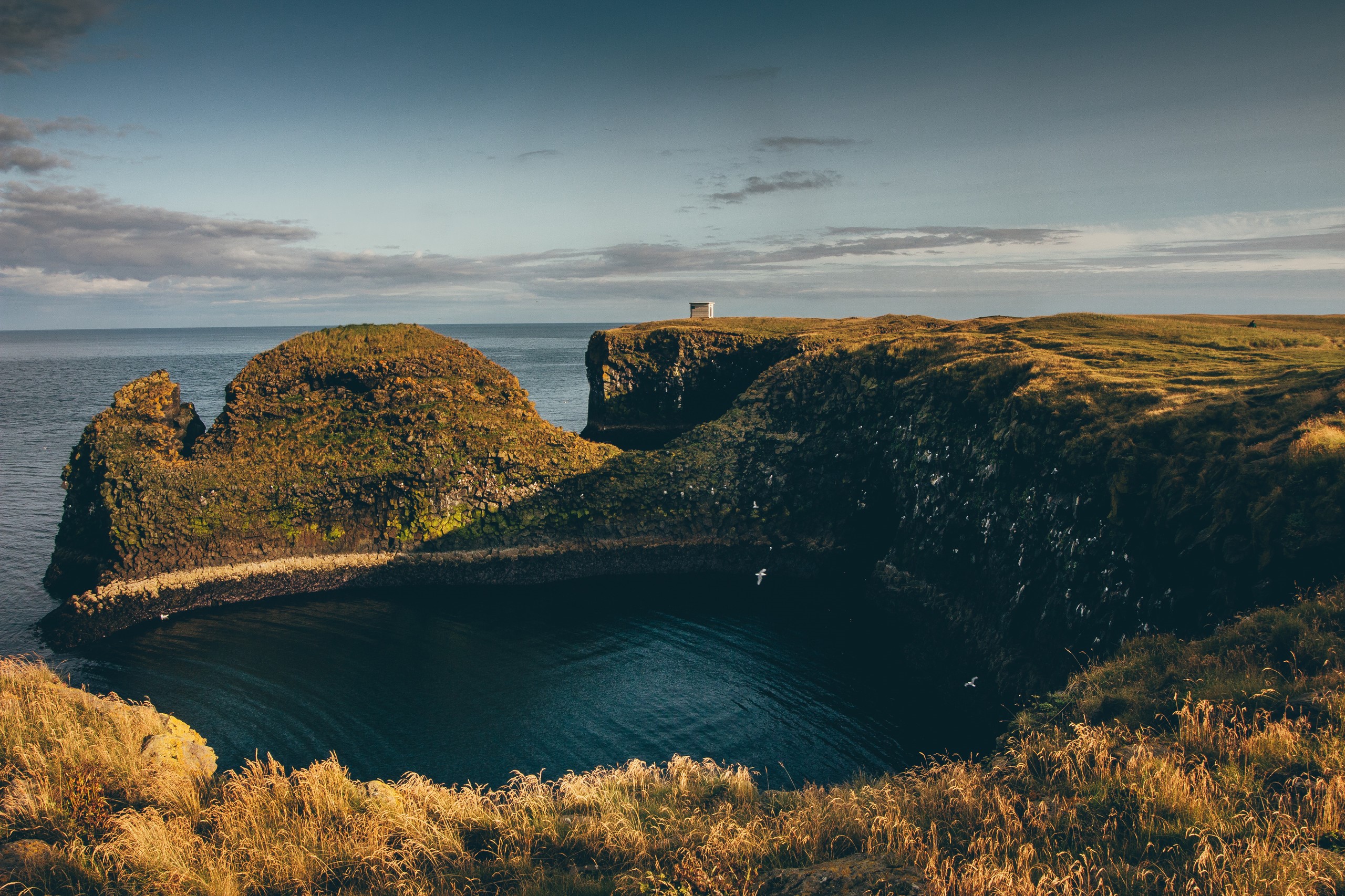 Coastal cliffs overlooking the sea with a small building on top HD Wallpaper