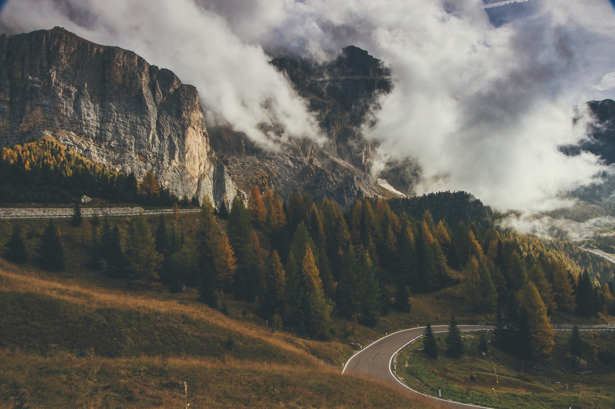 Mountain road winding through autumn trees with clouds HD Wallpaper