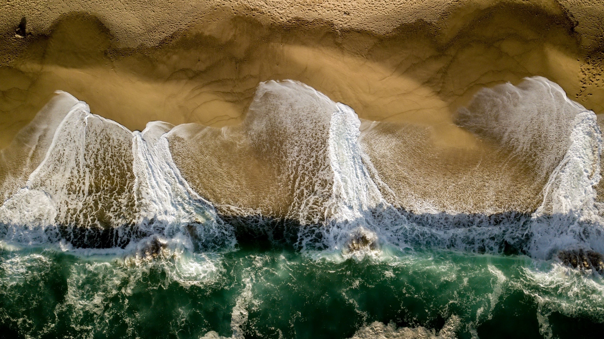 Aerial view of waves crashing on a sandy beach HD Wallpaper