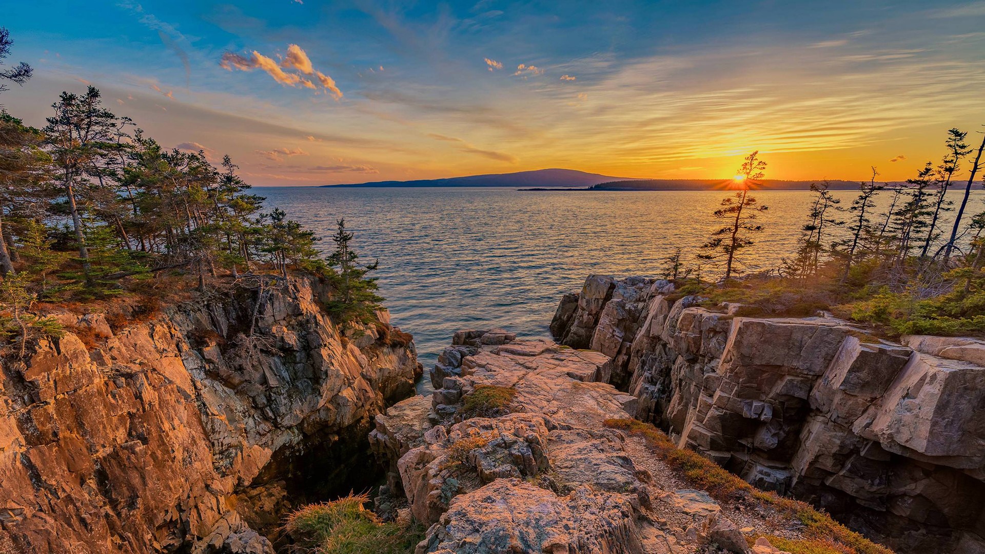 Rocky coastline at sunset with ocean and distant hills HD Wallpaper