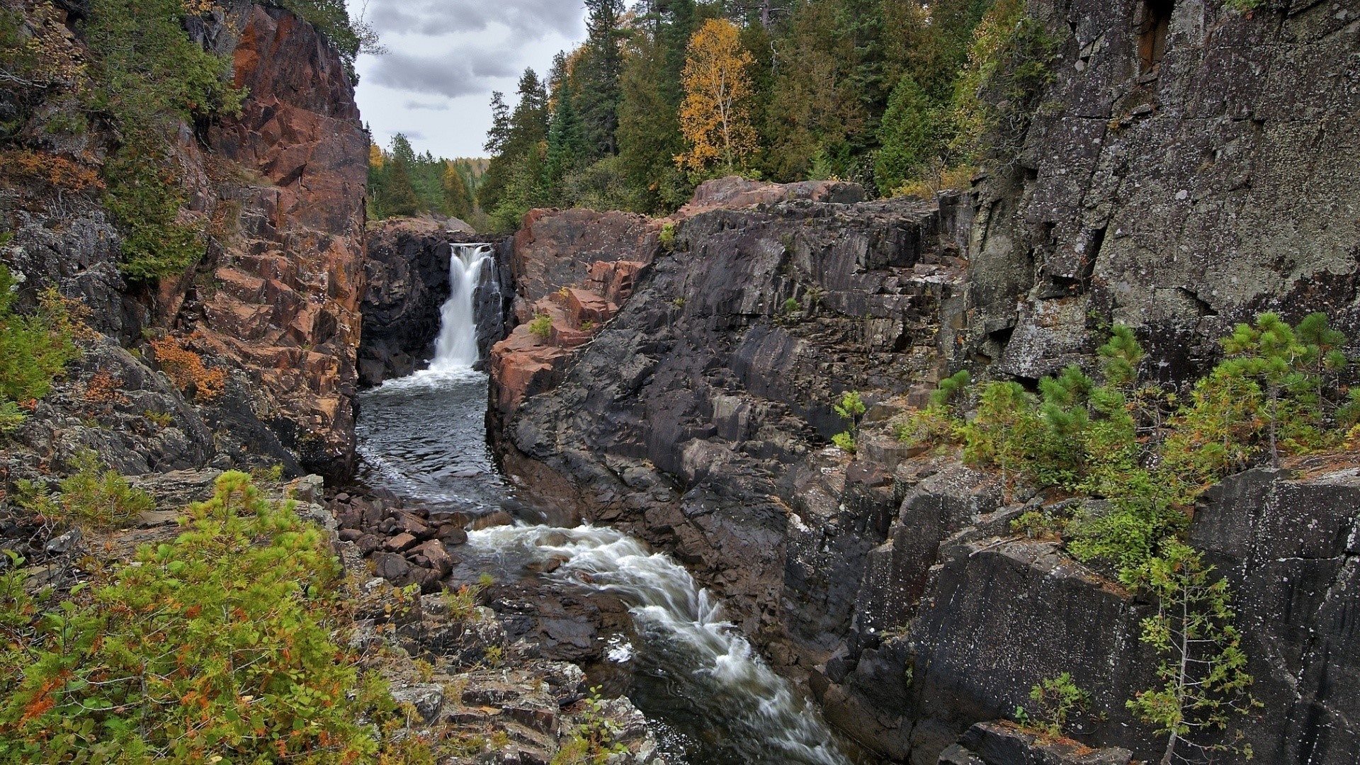 Waterfall cascading through rocky gorge with autumn trees HD Wallpaper
