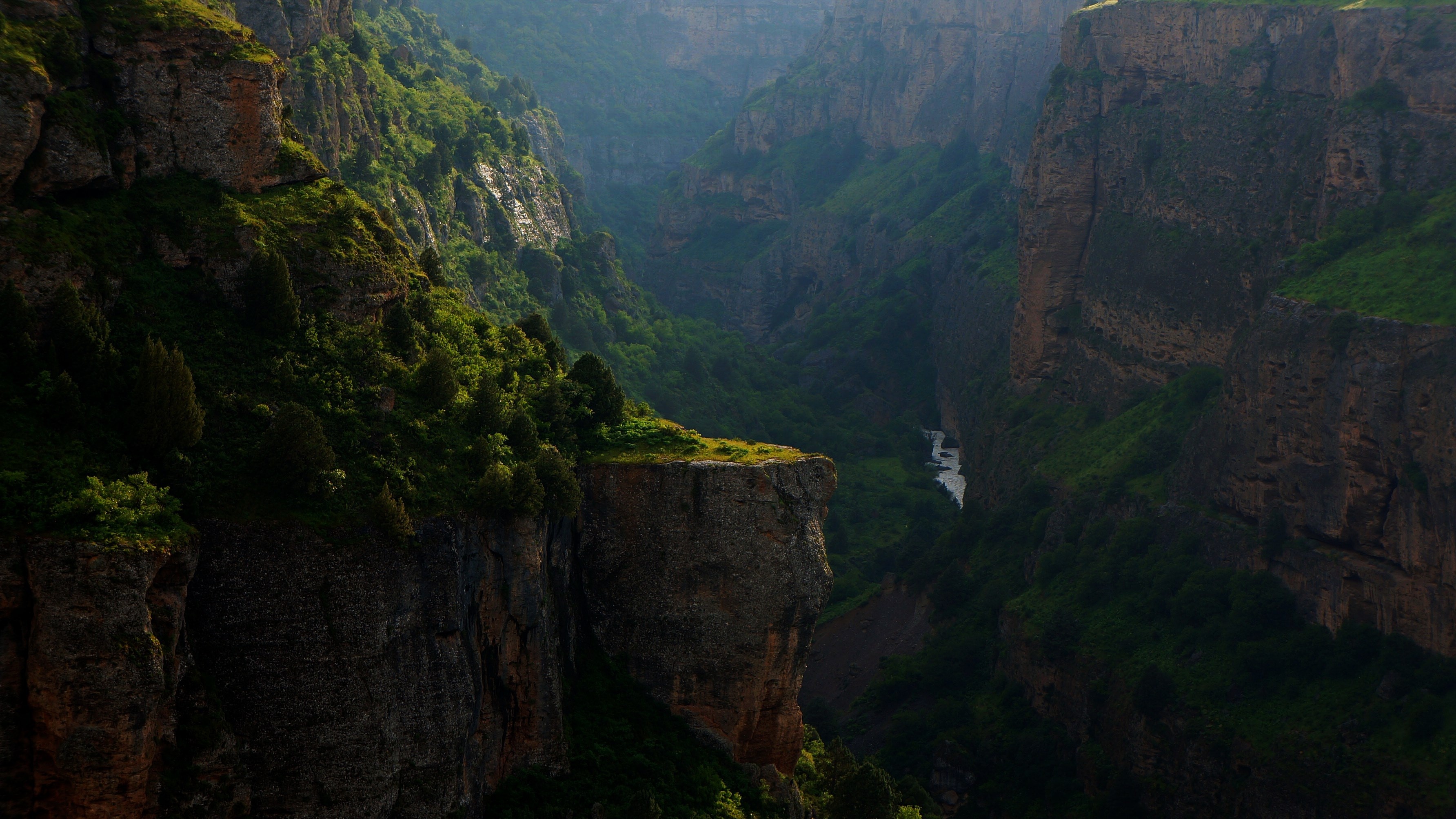 Sunlight illuminates a deep canyon with a river below HD Wallpaper
