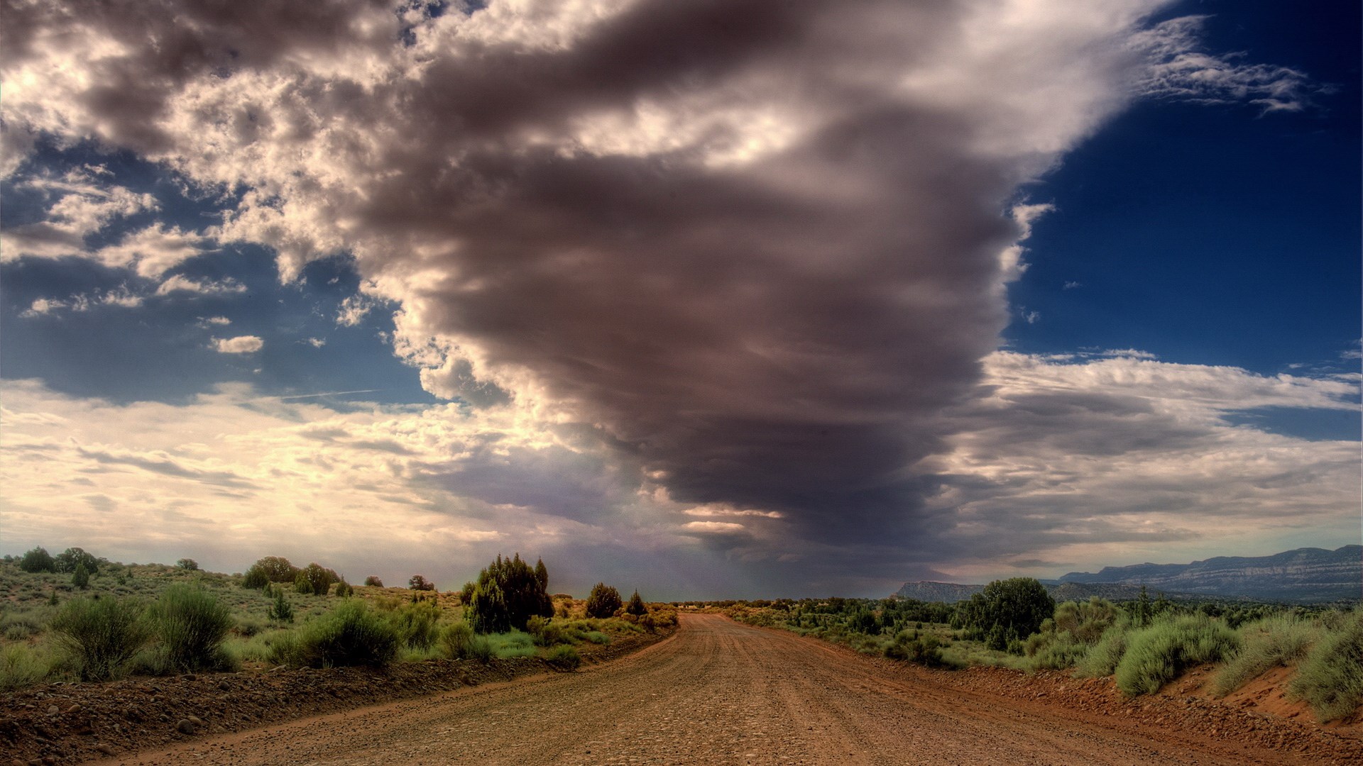 Dirt road through a desert landscape under stormy clouds HD Wallpaper