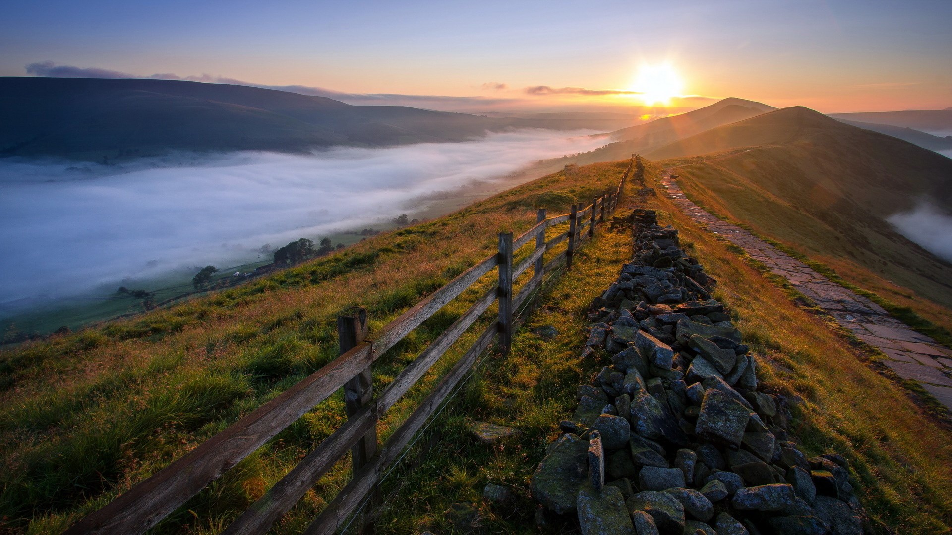 Sunrise over foggy mountains with a stone wall and fence HD Wallpaper