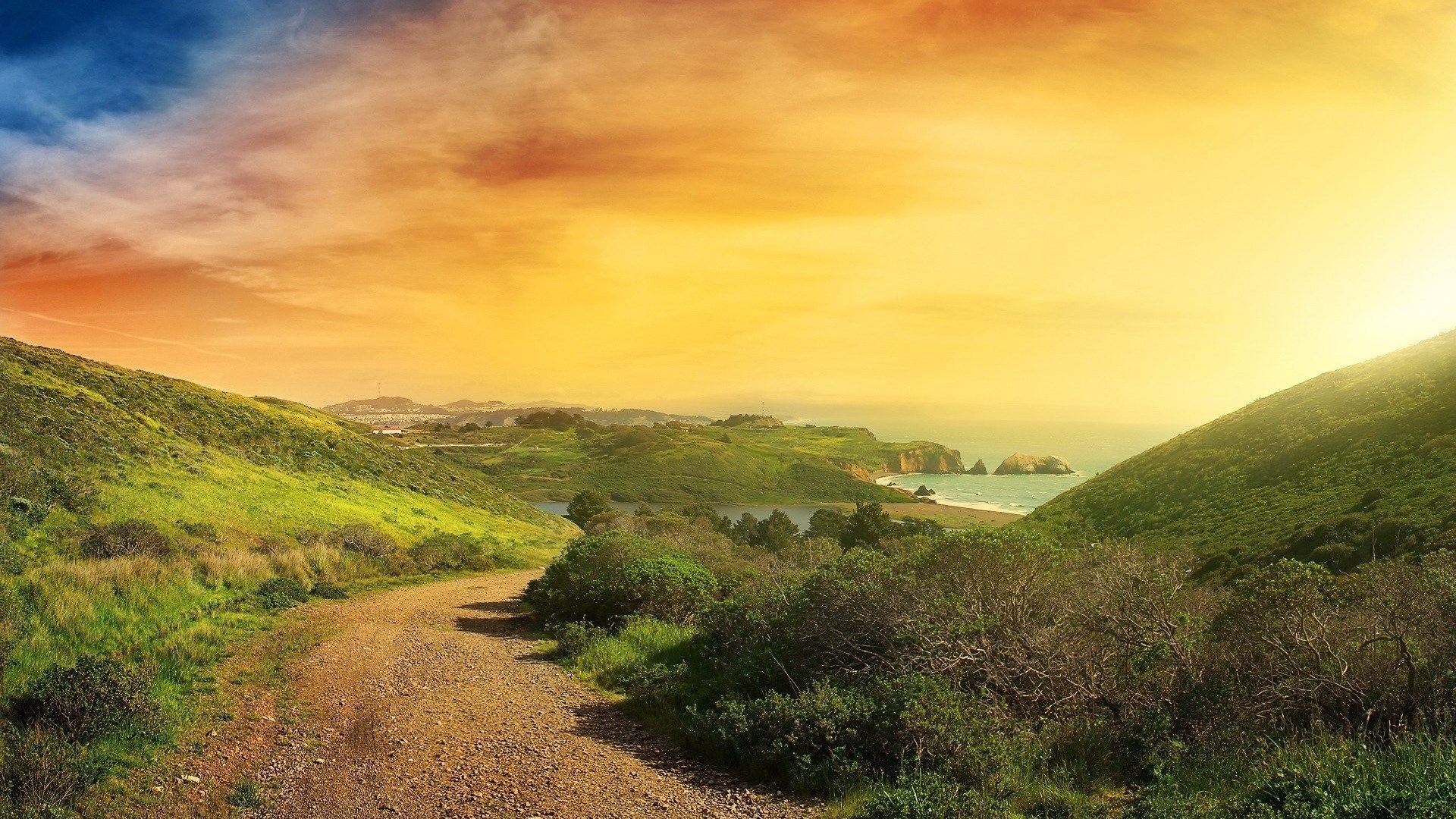 Dirt path through green hills towards the ocean at sunset HD Wallpaper