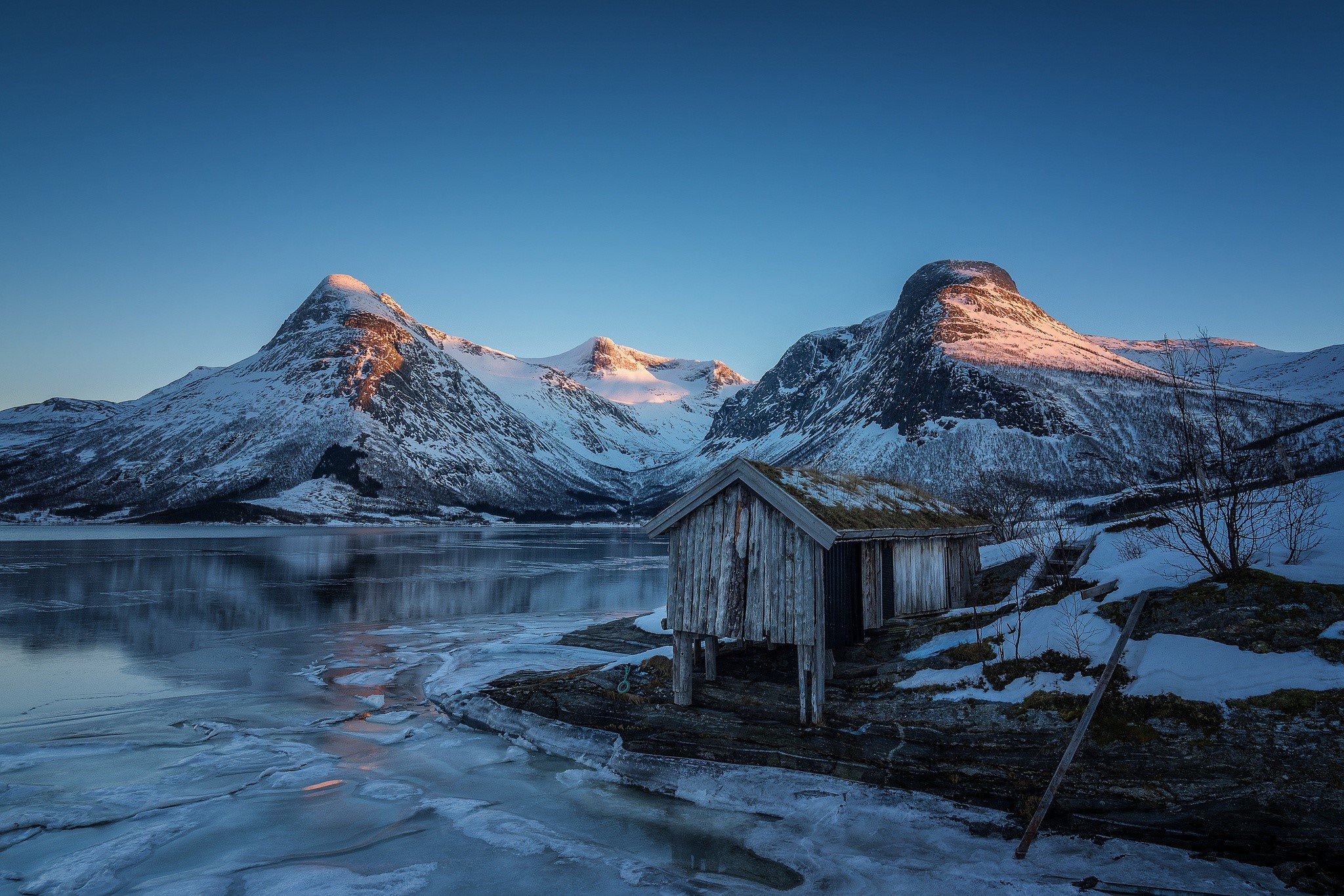 Snowy mountains and frozen lake with a small cabin in Norway HD Wallpaper
