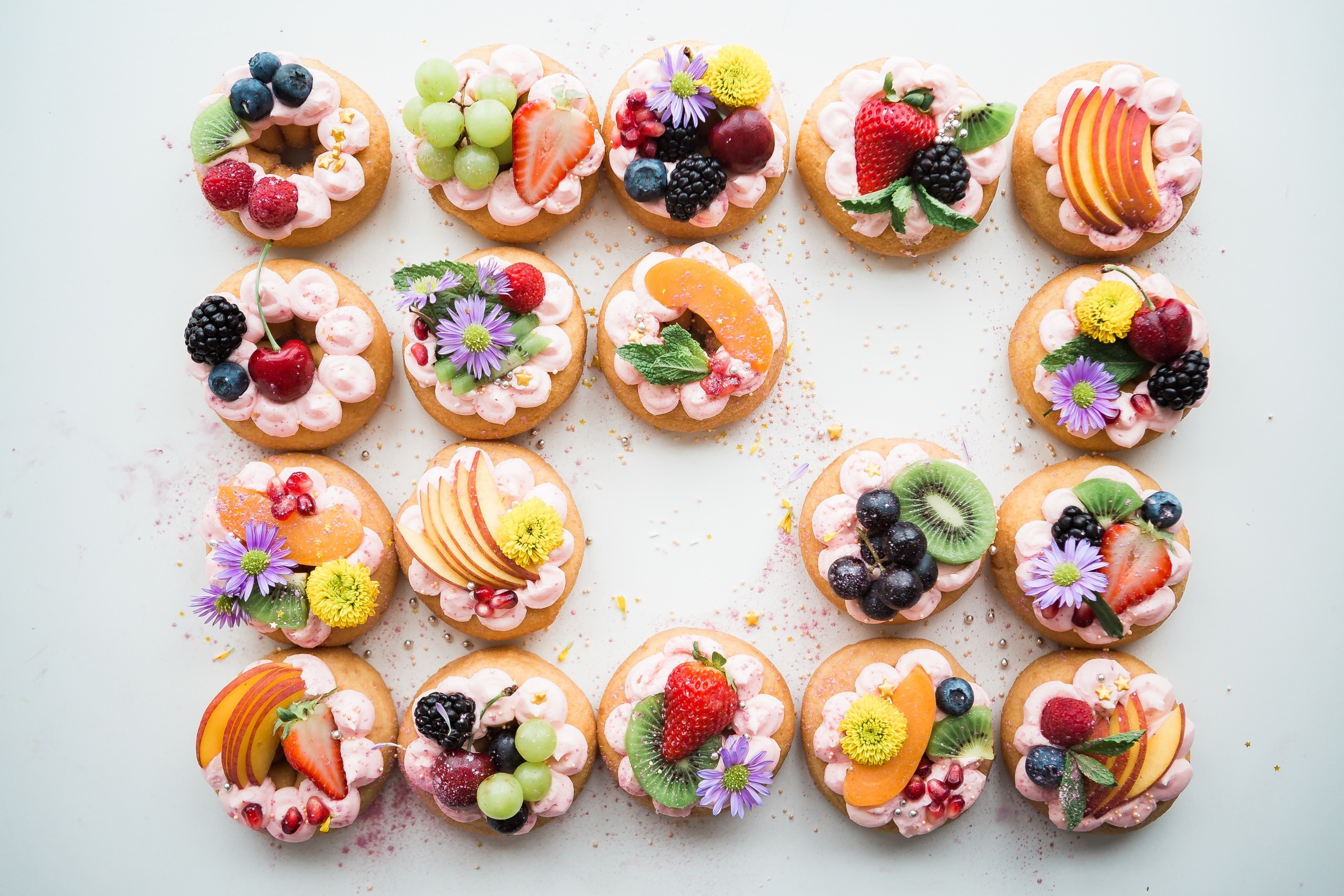 Assortment of decorated donuts with fresh fruit and flowers HD Wallpaper