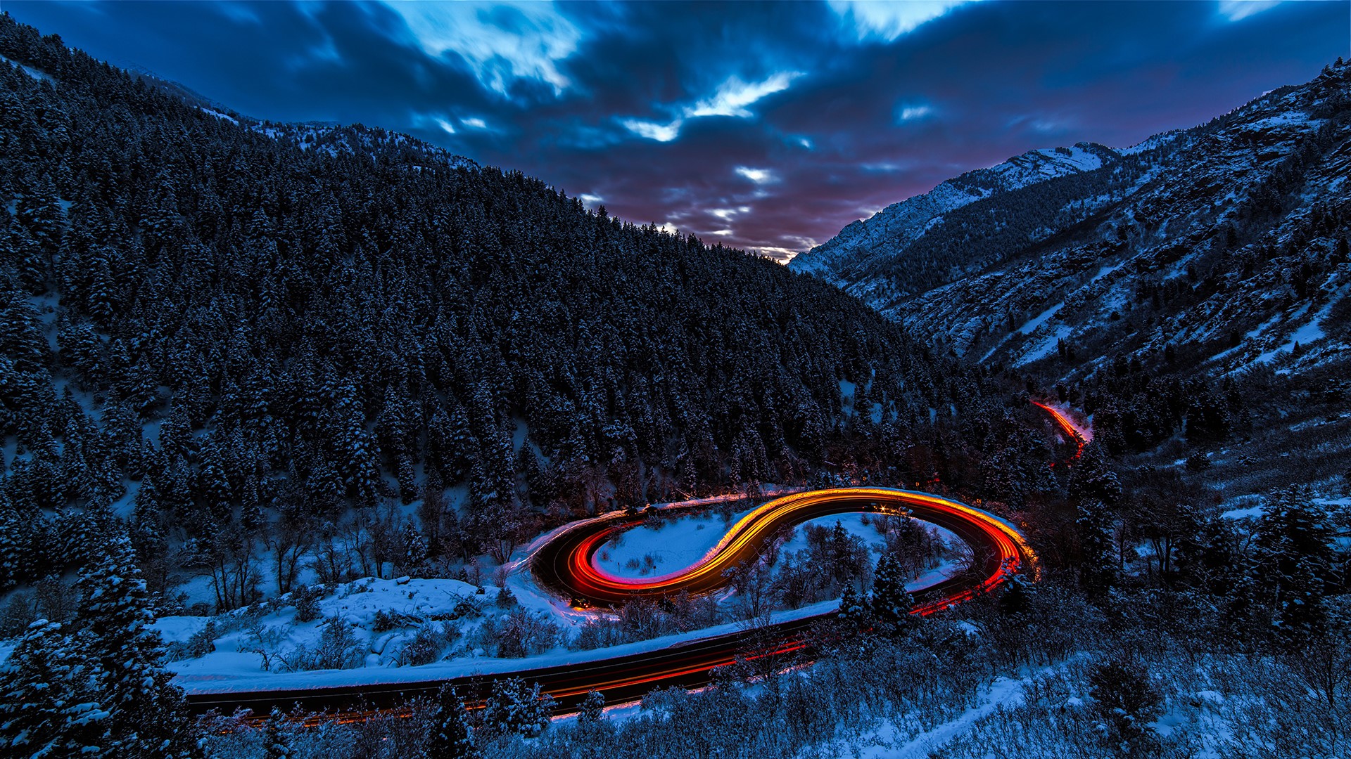 Light trails on a snowy mountain road at dusk HD Wallpaper