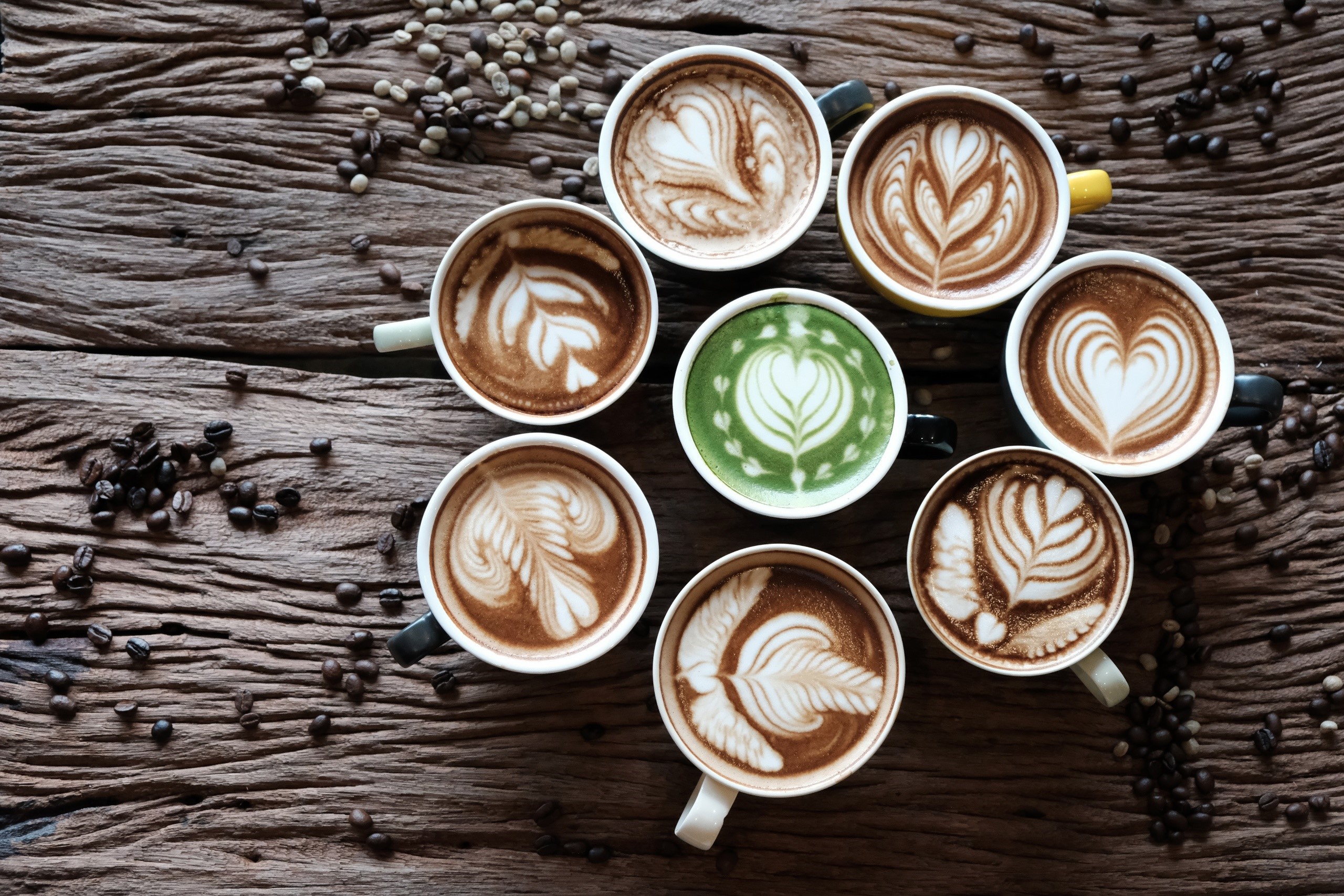 Latte art in cups with coffee beans on wooden table HD Wallpaper