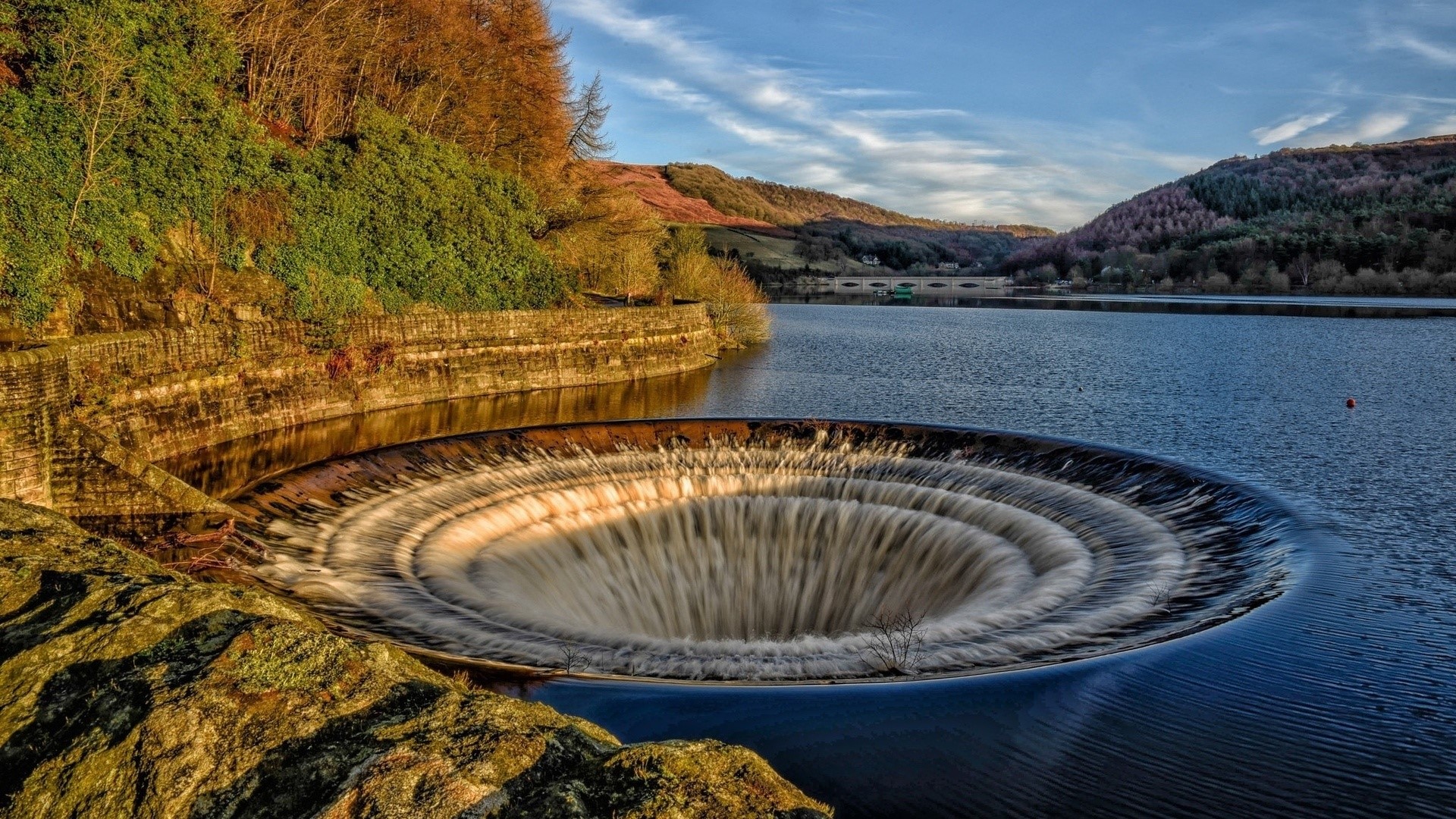 Circular overflow drain in a reservoir with hills in the background HD Wallpaper